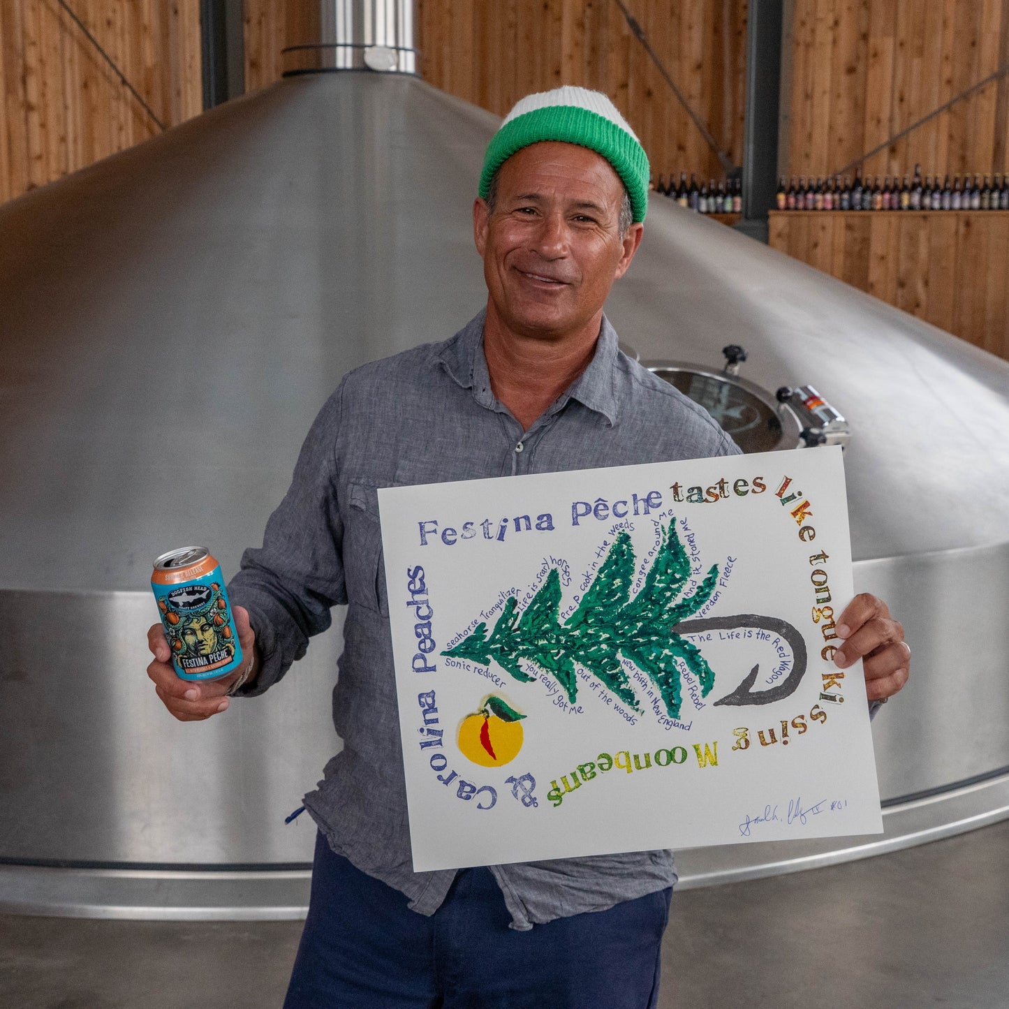 Festina Peche screen print poster displayed in a brewery setting, with a person holding both the handmade print and a Festina Peche beer can in front of stainless steel tanks.