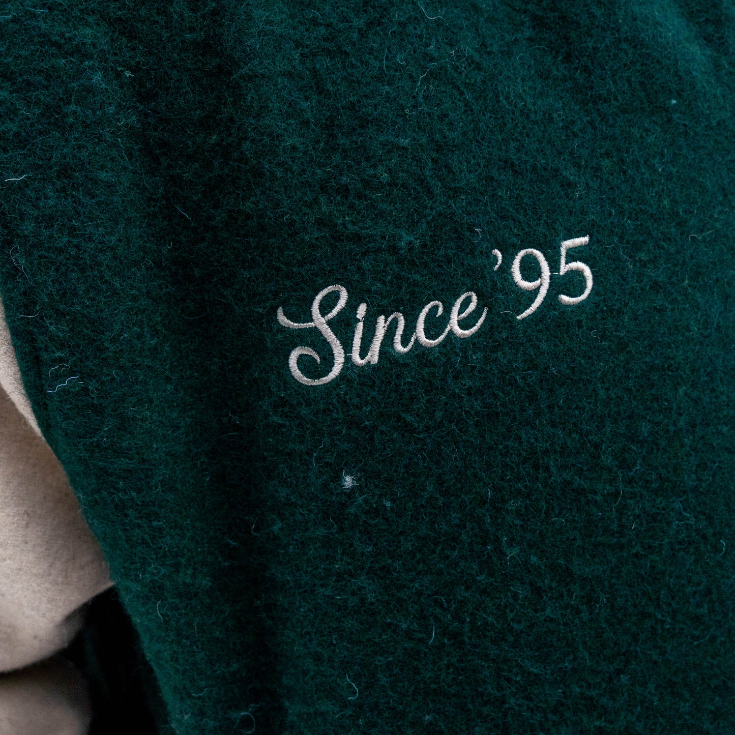 The Bottoms Up Varsity Jacket 2 features dark green textured fabric with "Since 95" embroidered in white script.
