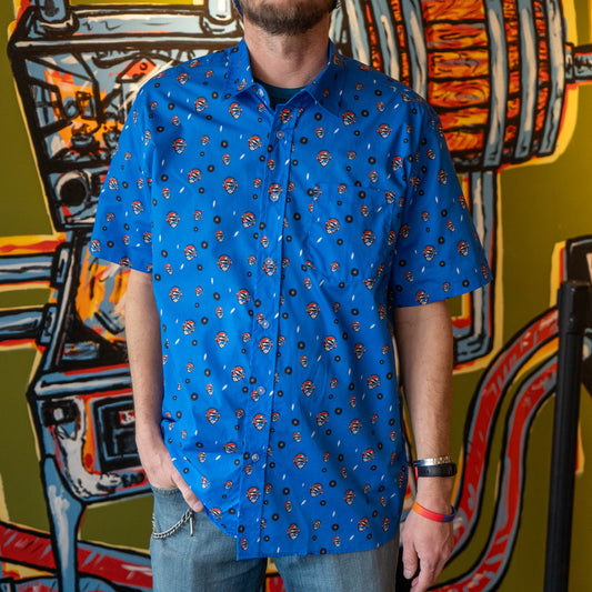 Man wearing a blue Dogfish Head x Grateful Dead button down shirt, designed in small lightning bolts, records, and Dogfish Head x Grateful dead red, white, and blue logos.