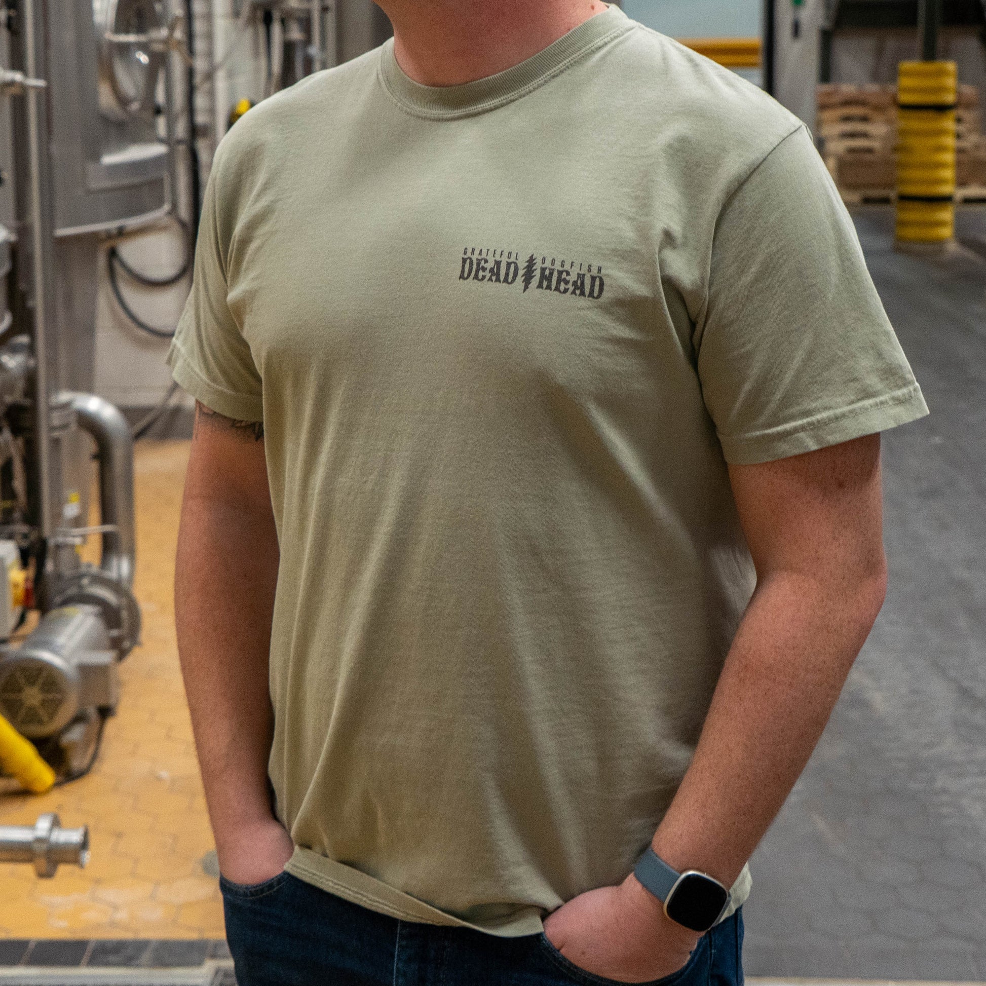 Front view of Dogfish Head x Grateful Dead Citrus Daydream Tee in the color sand. The front left chest has a logo in dark grey color reading "Grateful Dead, Dogfish Head" with a grateful dead lightning bolt symbol dividing the two logos. 