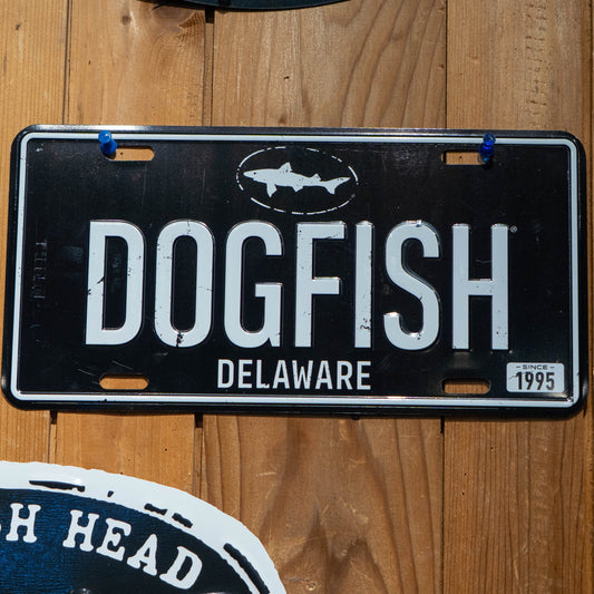 The Merchtank Black DOGFISH License Plate Tacker features a black and white metal design with "DOGFISH DELAWARE," a fish logo, and "SINCE 1995" in the corner—ideal for Delaware beer fans.
