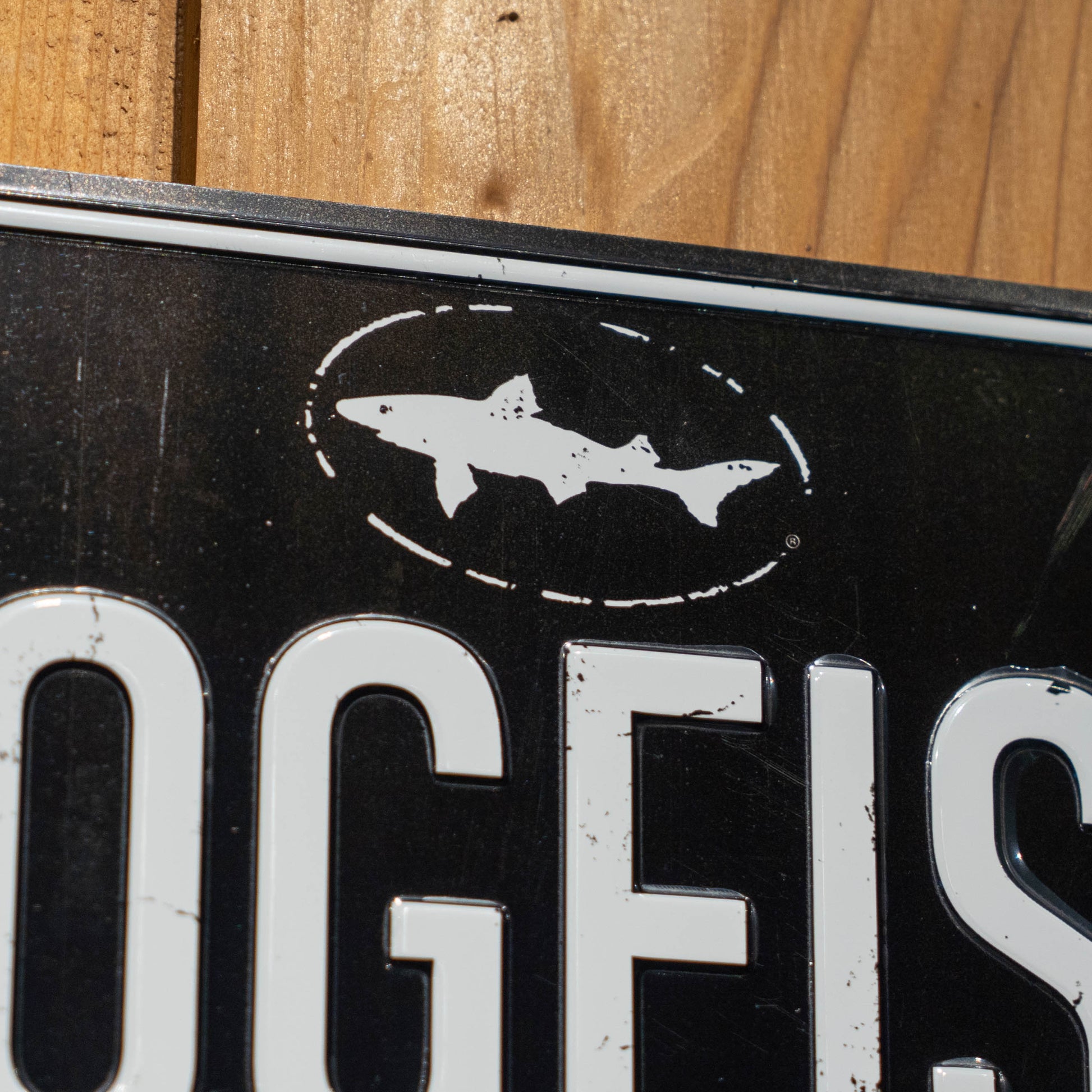 A close-up of the Black DOGFISH License Plate Tacker by Merchtank, featuring a white dogfish silhouette in an oval and white lettering—ideal wall décor for any Delaware beer lover.