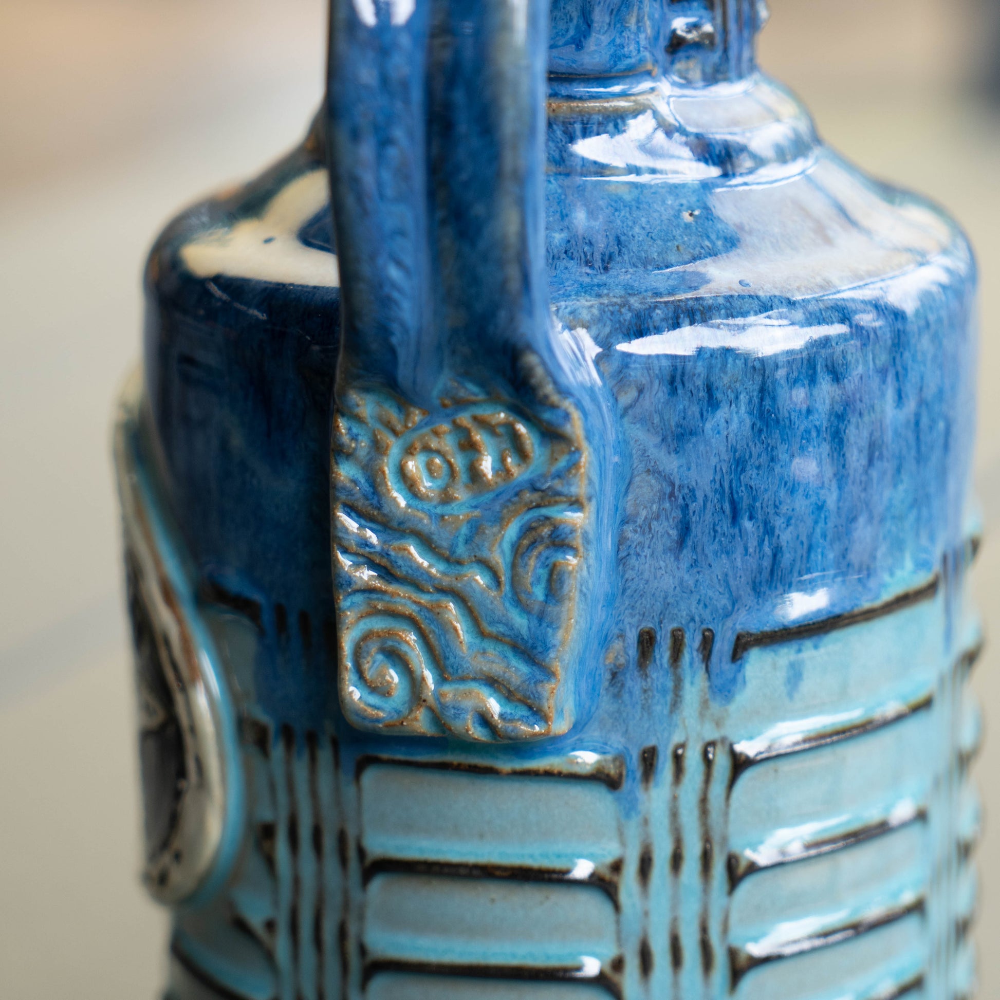 Close-up of the Blue Gradient Ceramic Growler by Romanick Pottery, featuring a glossy blue finish, textured horizontal ridges, and a handle embossed with decorative swirls and the letters OH.