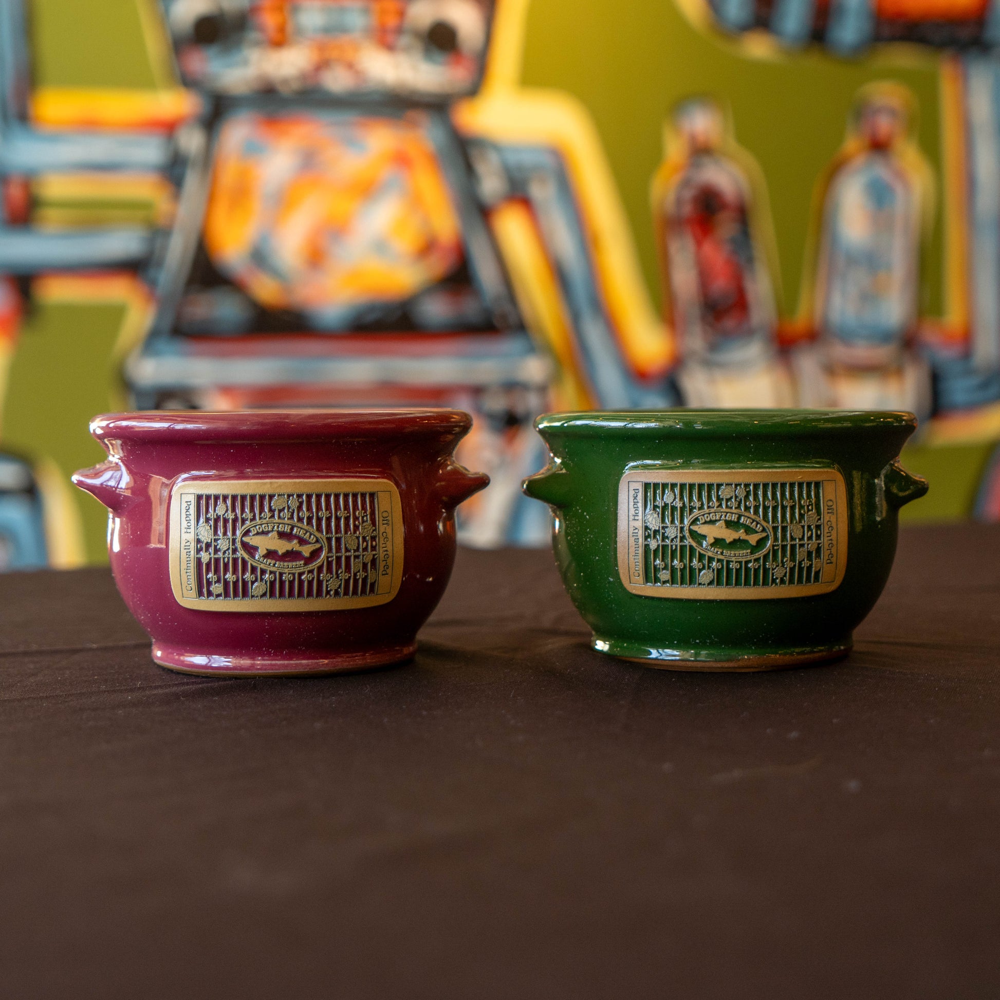 Two ceramic crocks with decorative labels on a dark surface, colorful background.