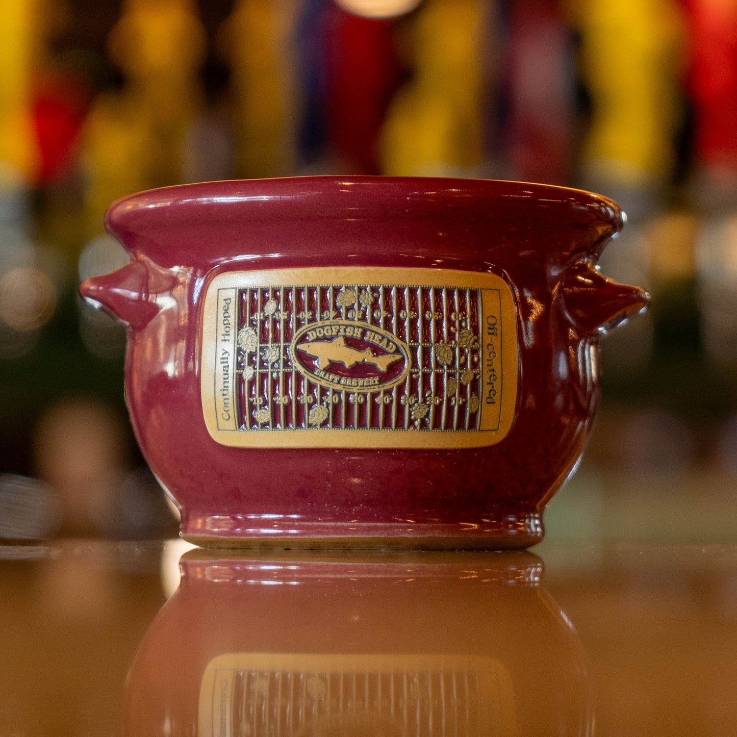 Red ceramic crock with a taupe label on a reflective surface, blurred background