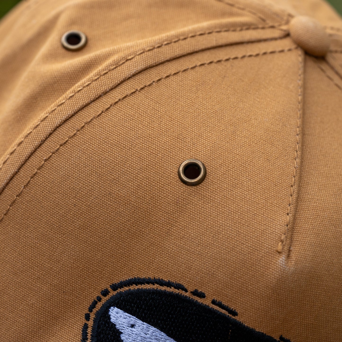 Close-up of the Brown Richardson Five Panel Snapback by Mirror Image Inc. highlights its tan color, detailed stitching, metal eyelets for ventilation, and a partial black and white shark embroidery near the brim.