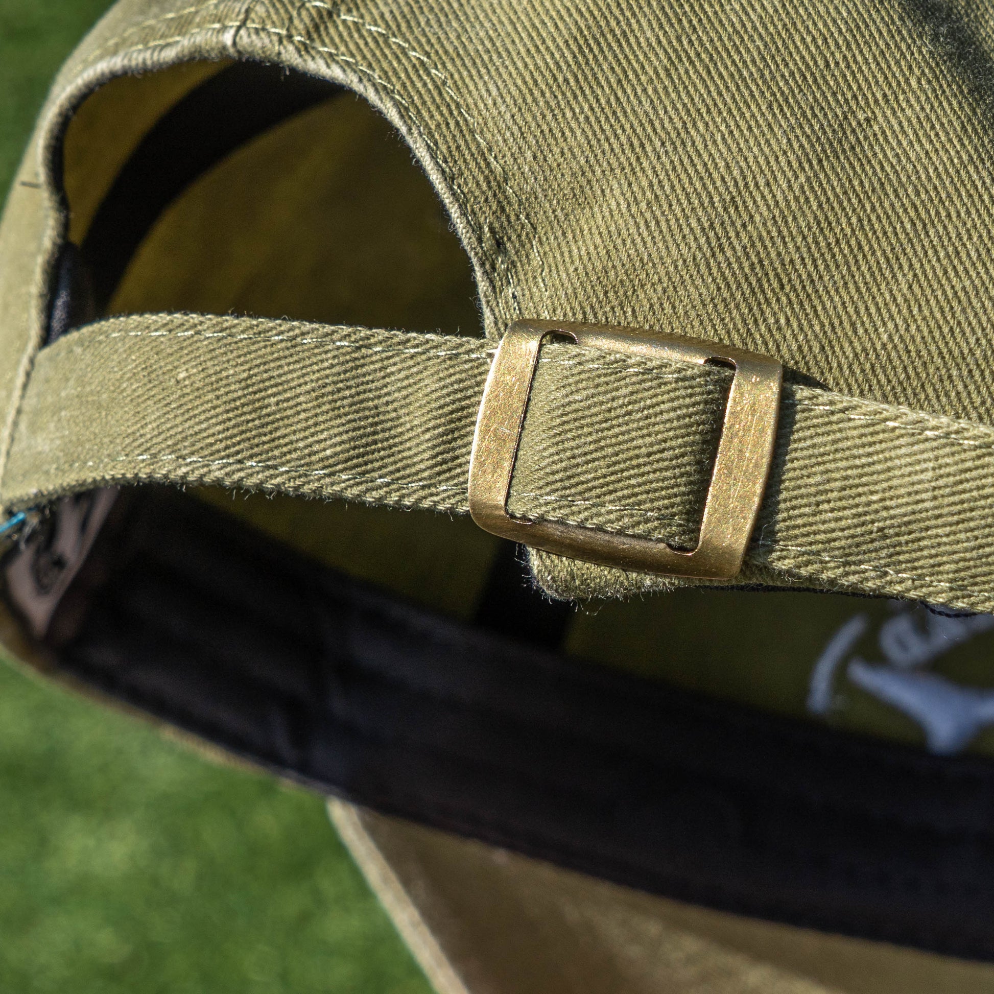 Close up of gold colored metal buckle on the adjustable strap of an olive-colored dad hat 