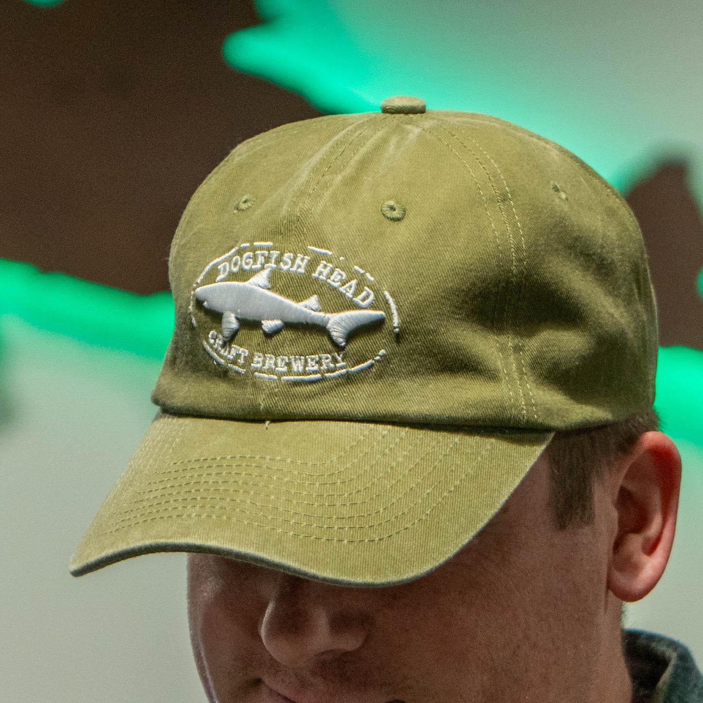 Man wearing an olive colored dad hat with a white Dogfish Head Craft Brewery embroidered logo.
