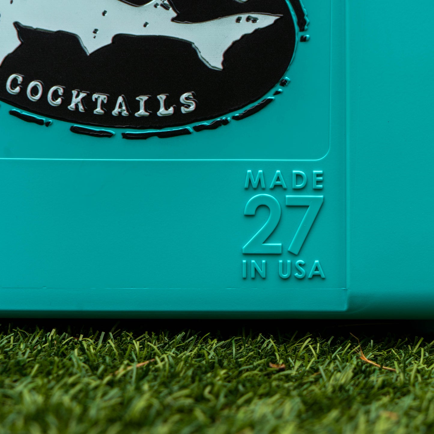 Teal container with 'COCKTAILS' and 'MADE 27 IN USA' text on grass
