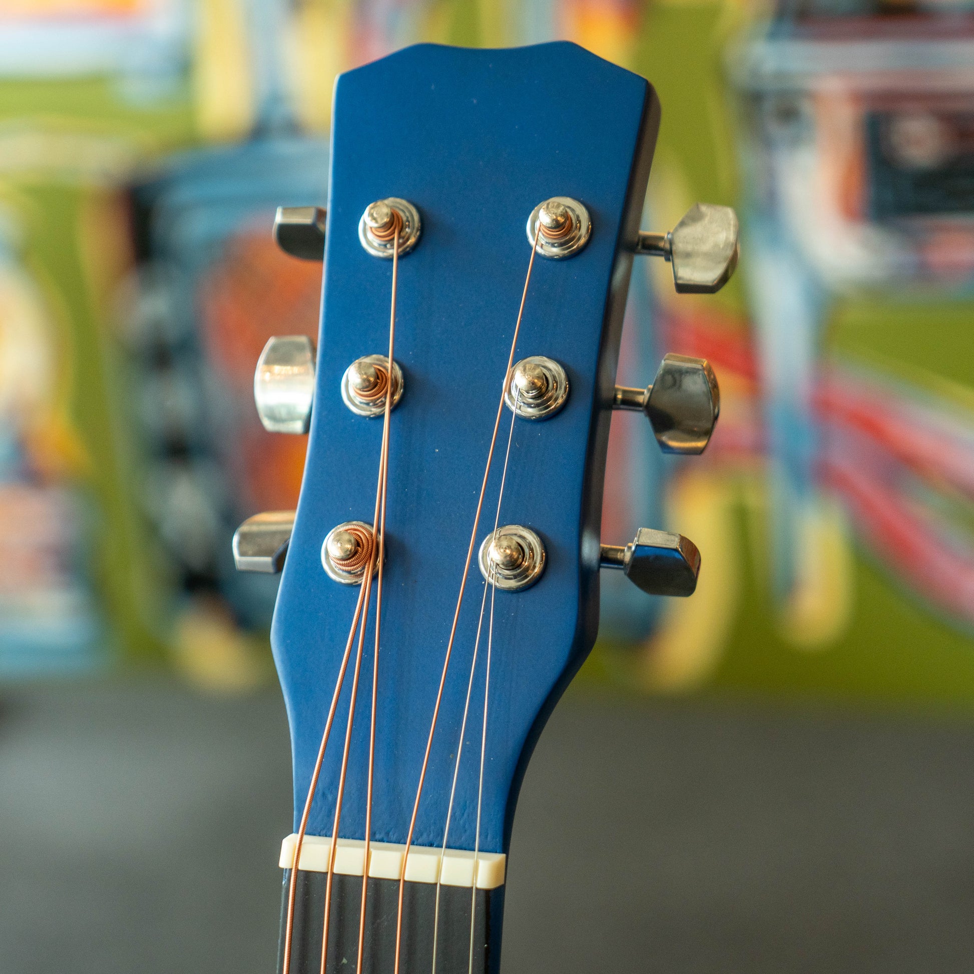 Close-up of a blue guitar headstock with colorful blurred background