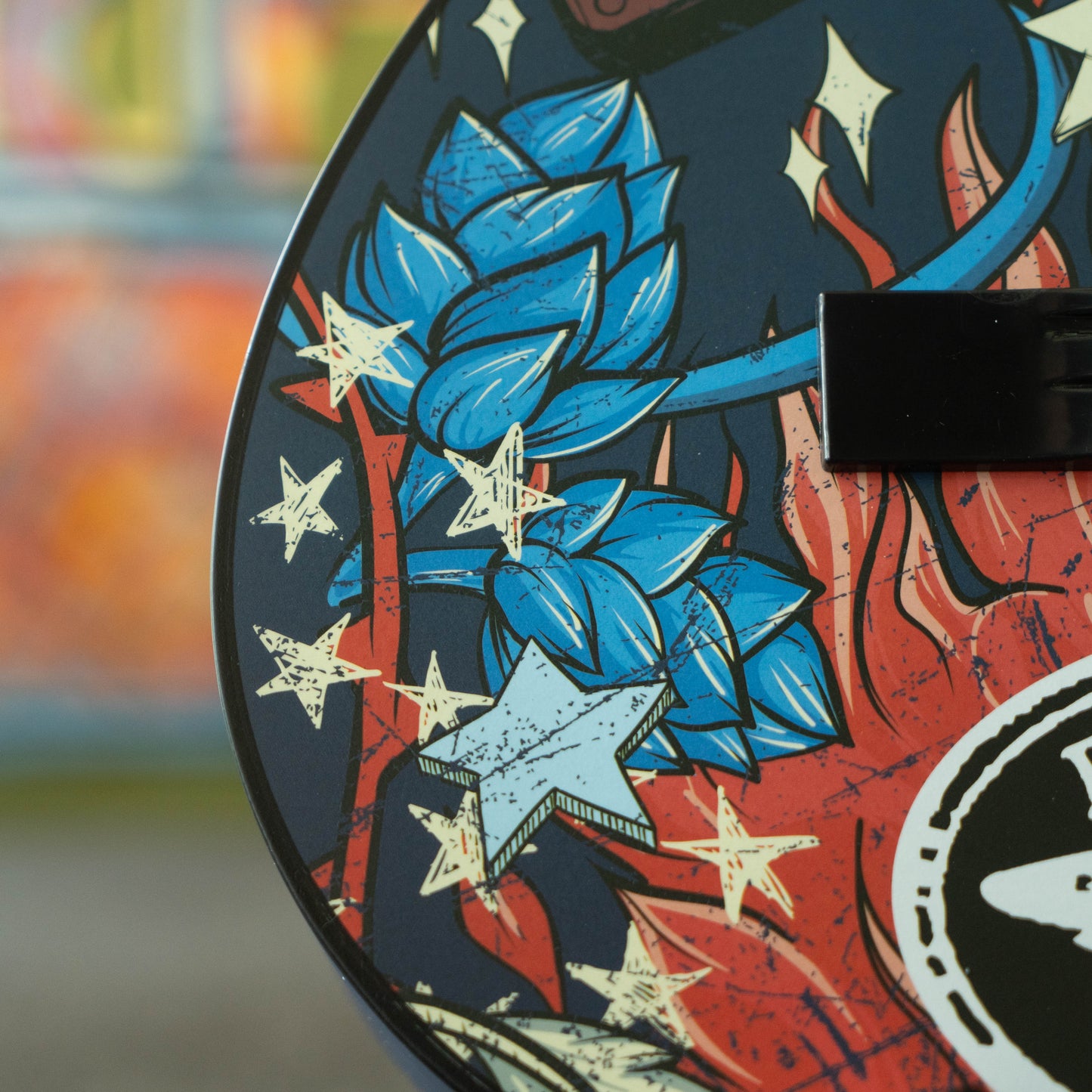 Close-up of a guitar deck with blue and red design featuring stars and abstract shapes.
