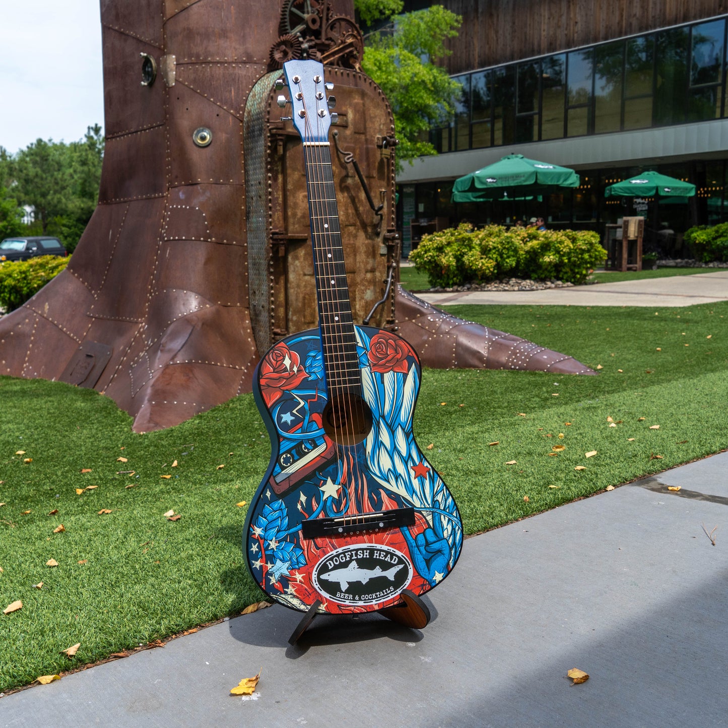 Colorful guitar sculpture on a stand with a building and greenery in the background
