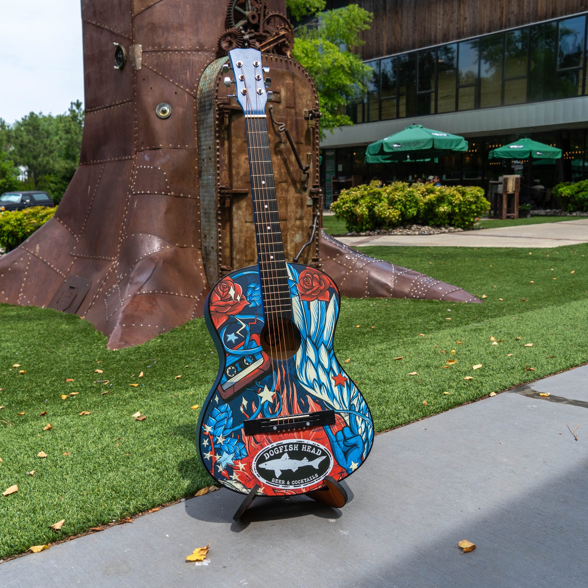 Colorful guitar sculpture on a stand with a building and greenery in the background