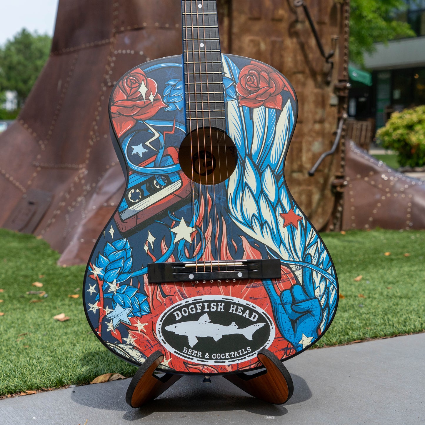 Decorative guitar with tattoo-style design on a stand outdoors.