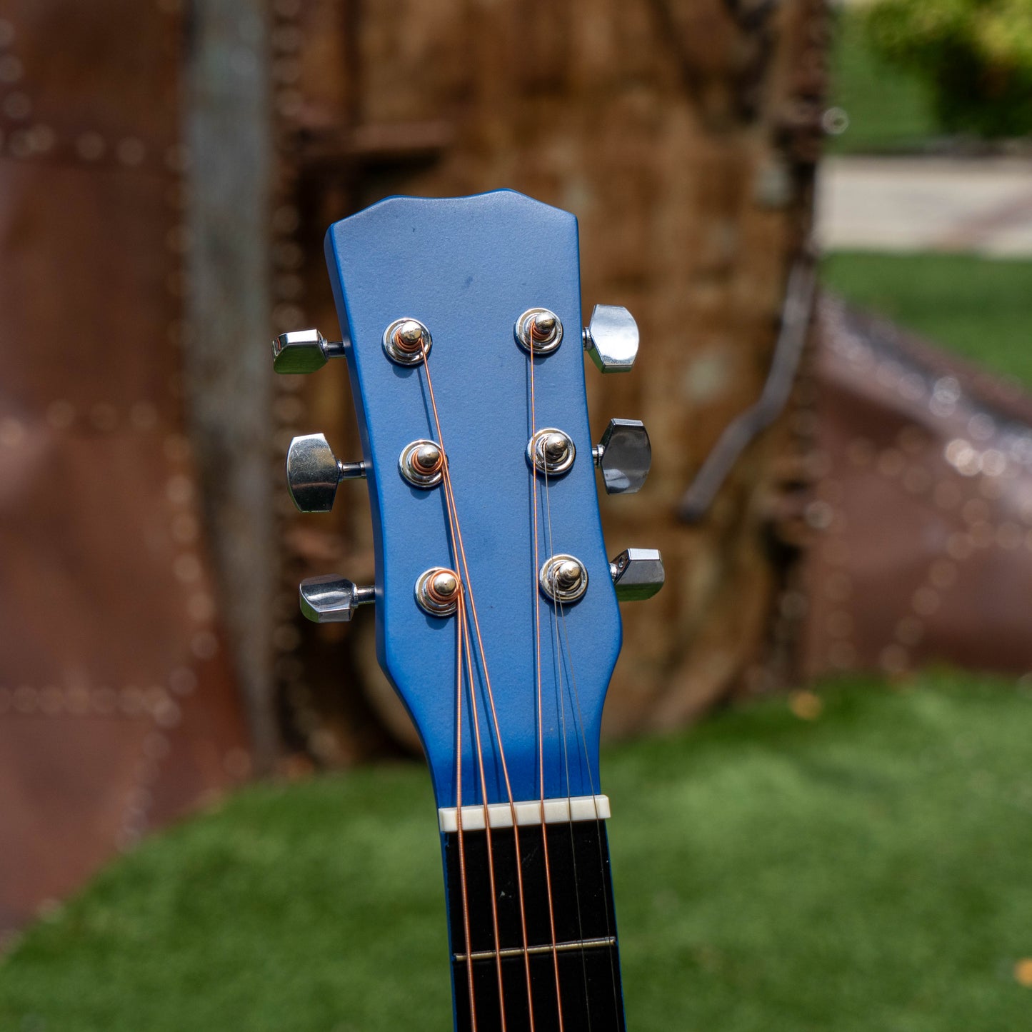 Close-up of a blue guitar headstock with blurred outdoor background