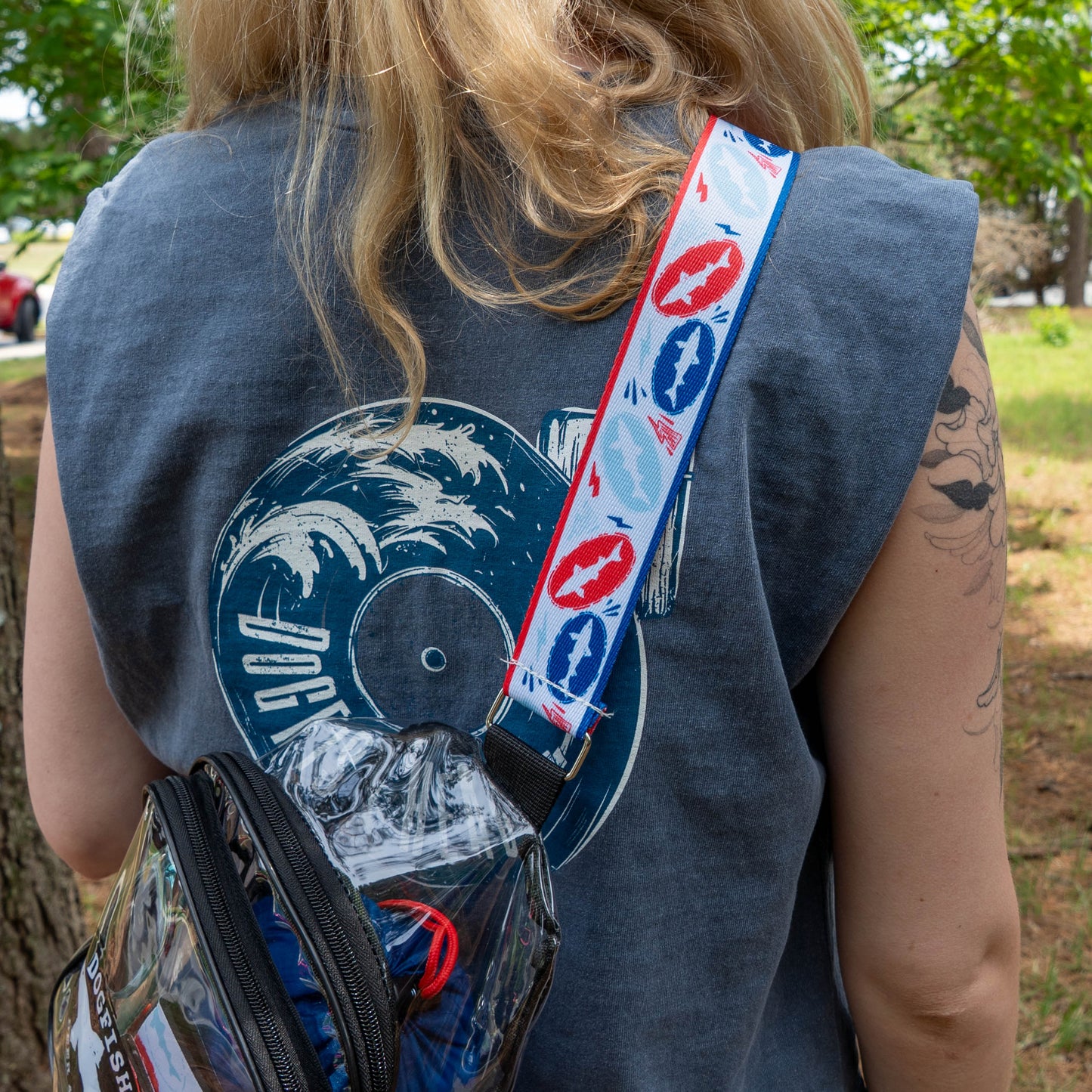 A person with long blonde hair rocks the Merchtank Drink Summer Louder Festival Kit—featuring a sleeveless shirt, see-through crossbody bag, and festival-ready accessories—for the ultimate summer vibe.