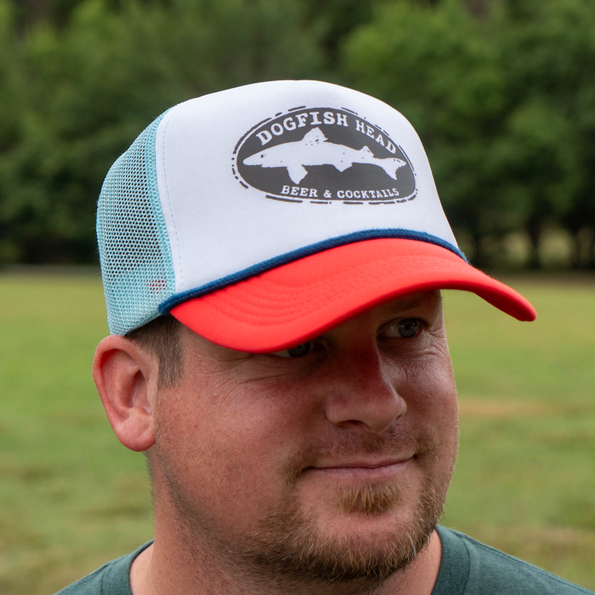 Man wearing a Dogfish Head cap outdoors with greenery in the background