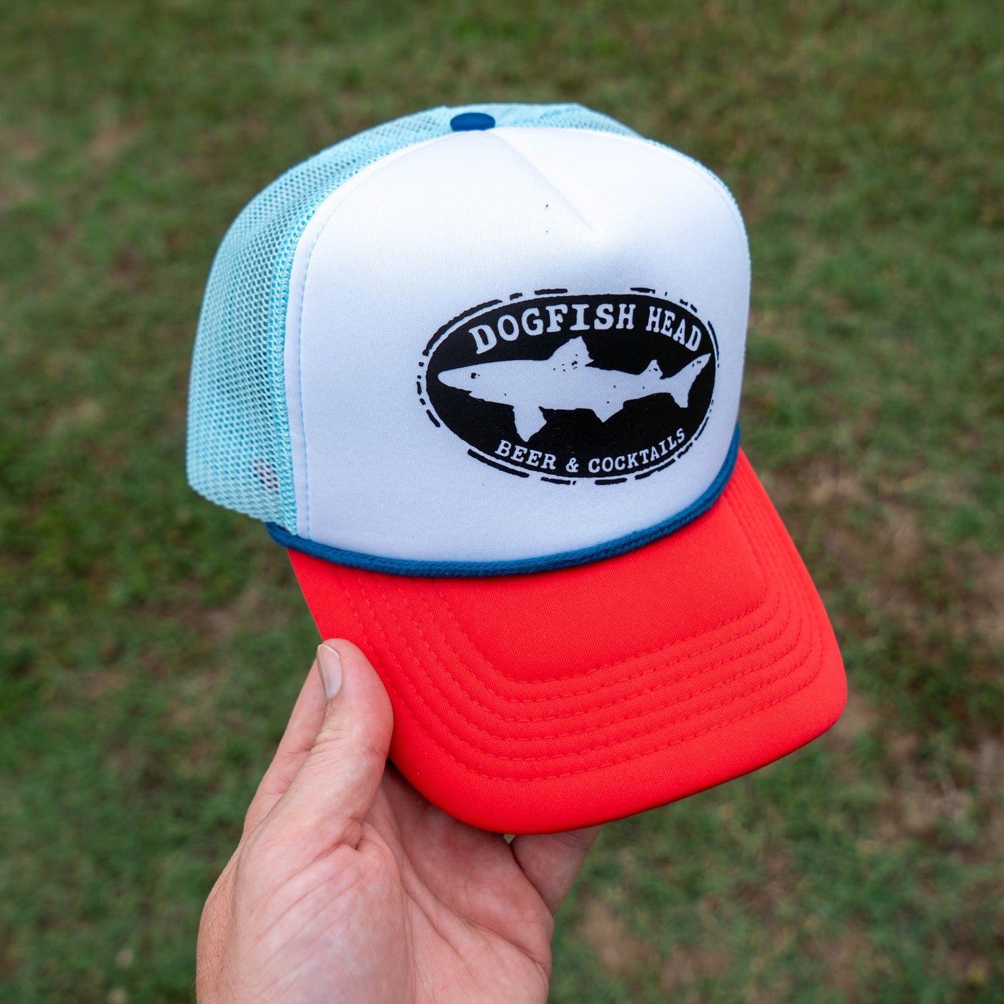 Trucker hat with 'Dogfish Head' logo held in front of a grassy background