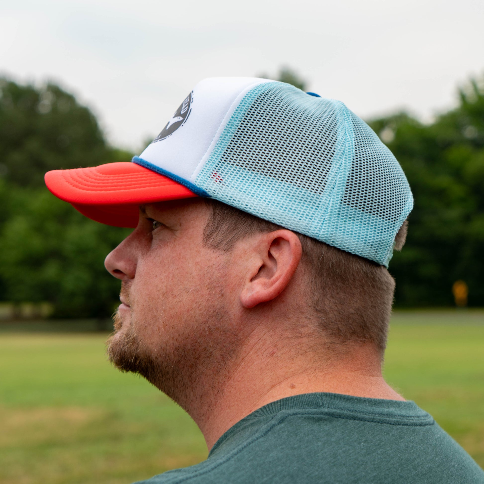 Man wearing a light blue and red cap outdoors with trees in the background