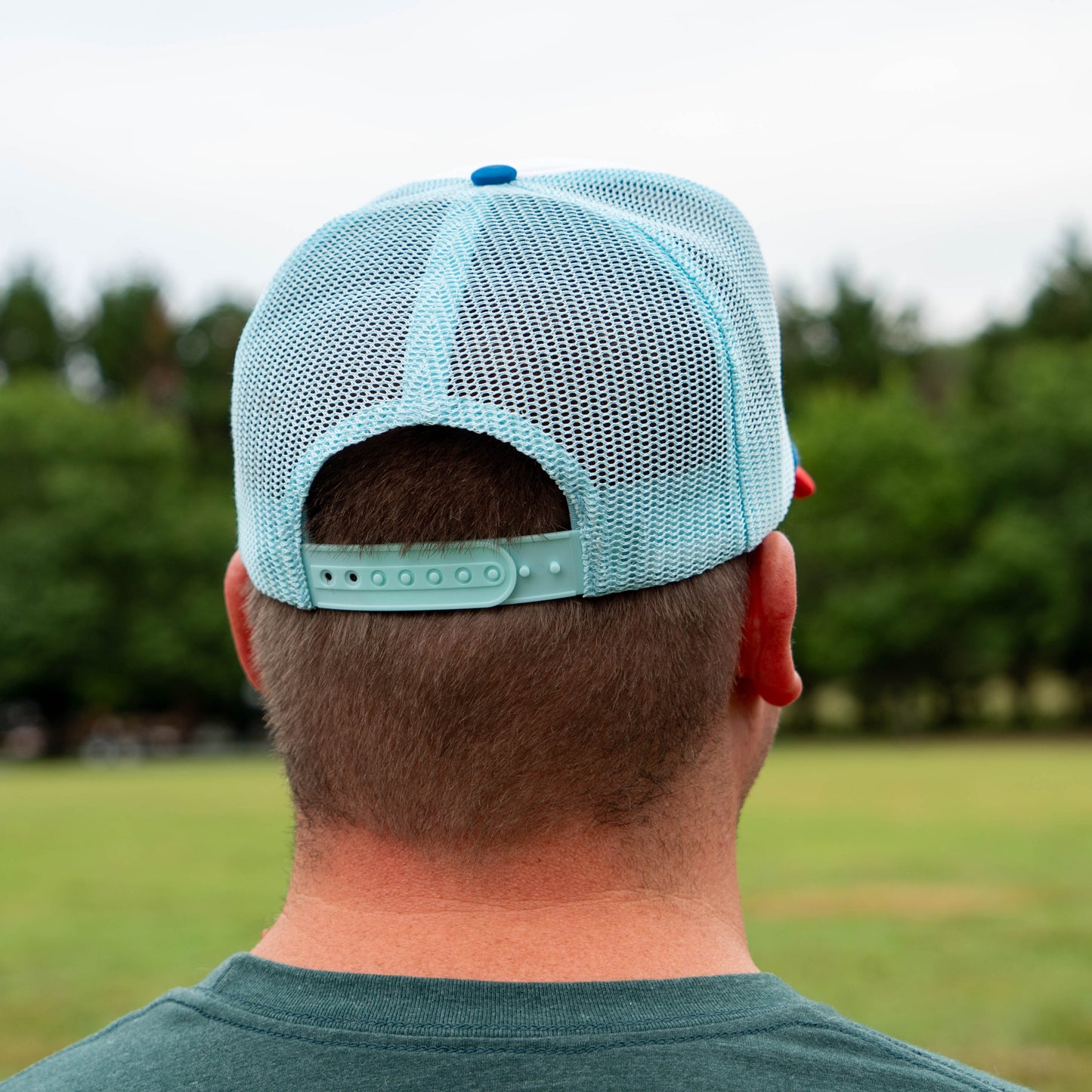 Person wearing a light blue mesh cap outdoors with greenery in the background