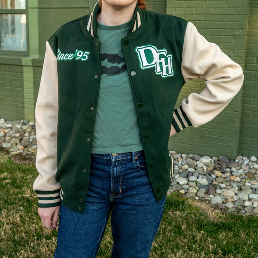 Person wearing a green and cream varsity jacket with 'DTH' letters, standing outdoors.