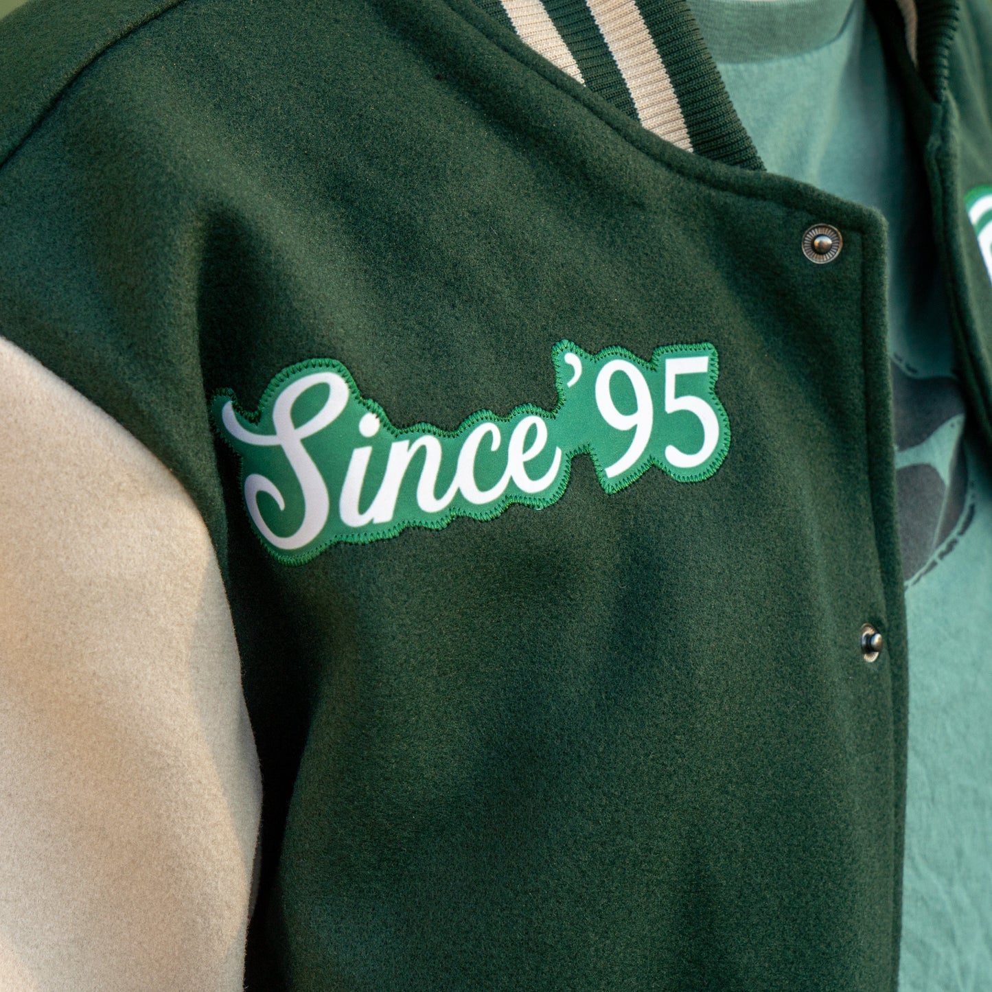 Green jacket with 'Since 95' patch on a person wearing a green shirt.
