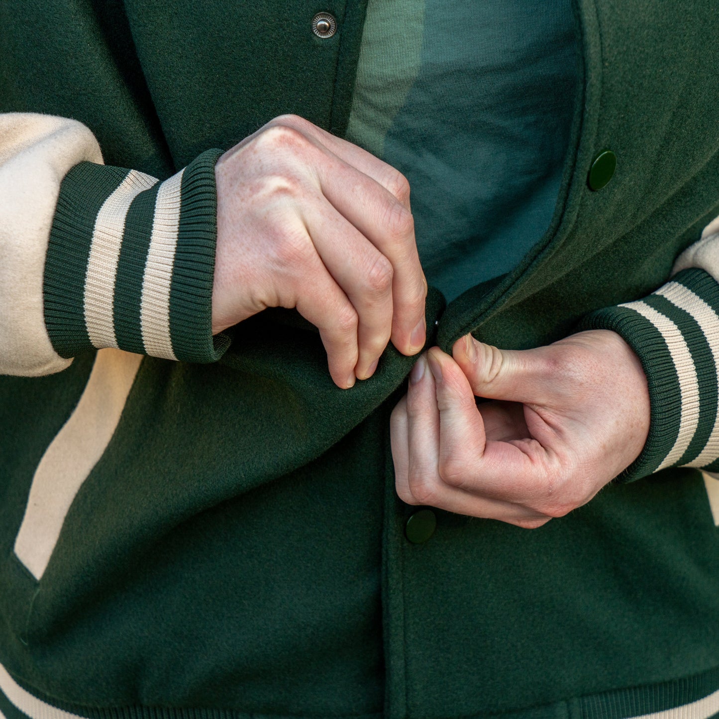 Person buttoning a green jacket with white and green striped sleeves.