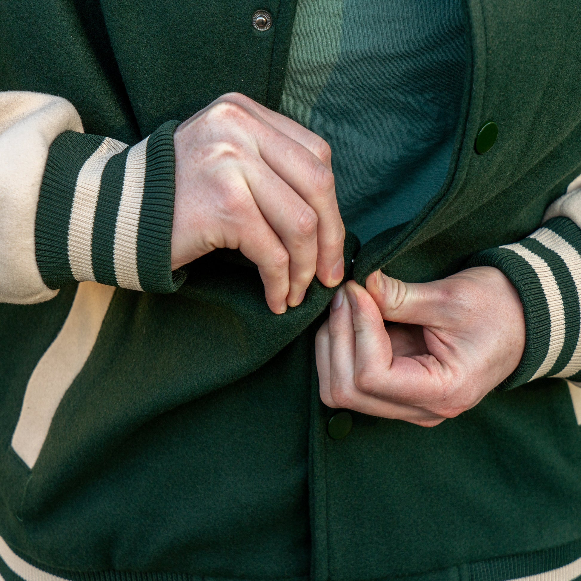 Person buttoning a green jacket with white and green striped sleeves.