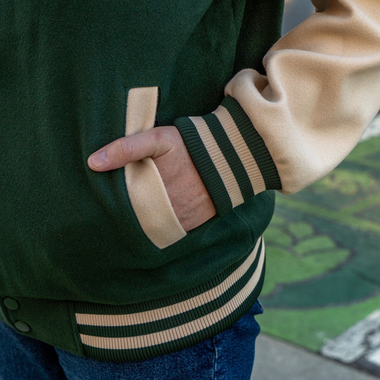 Close-up of a person wearing a green and beige varsity jacket with a blurred background