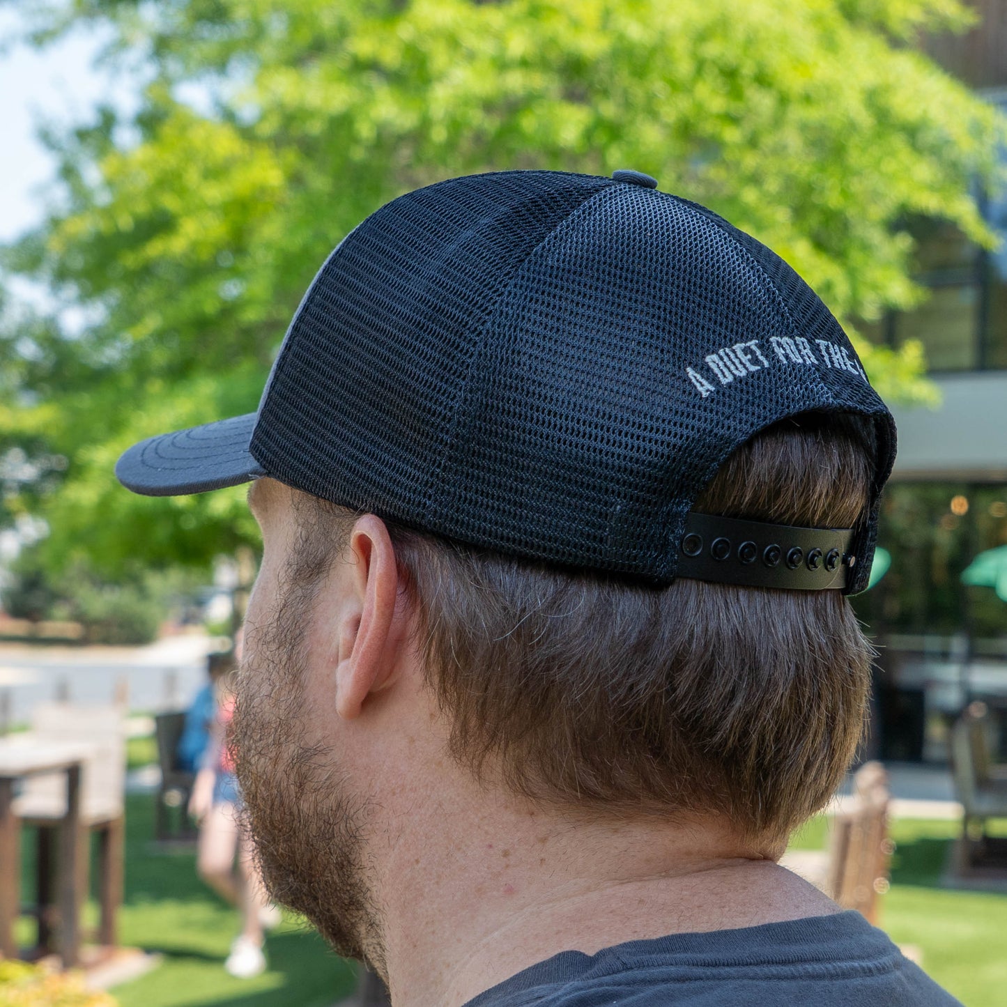 Person wearing a Dogfish Head x Rolling Stone trucker hat with black mesh back and snapback with 'A Duet For The Ages' text on the back
