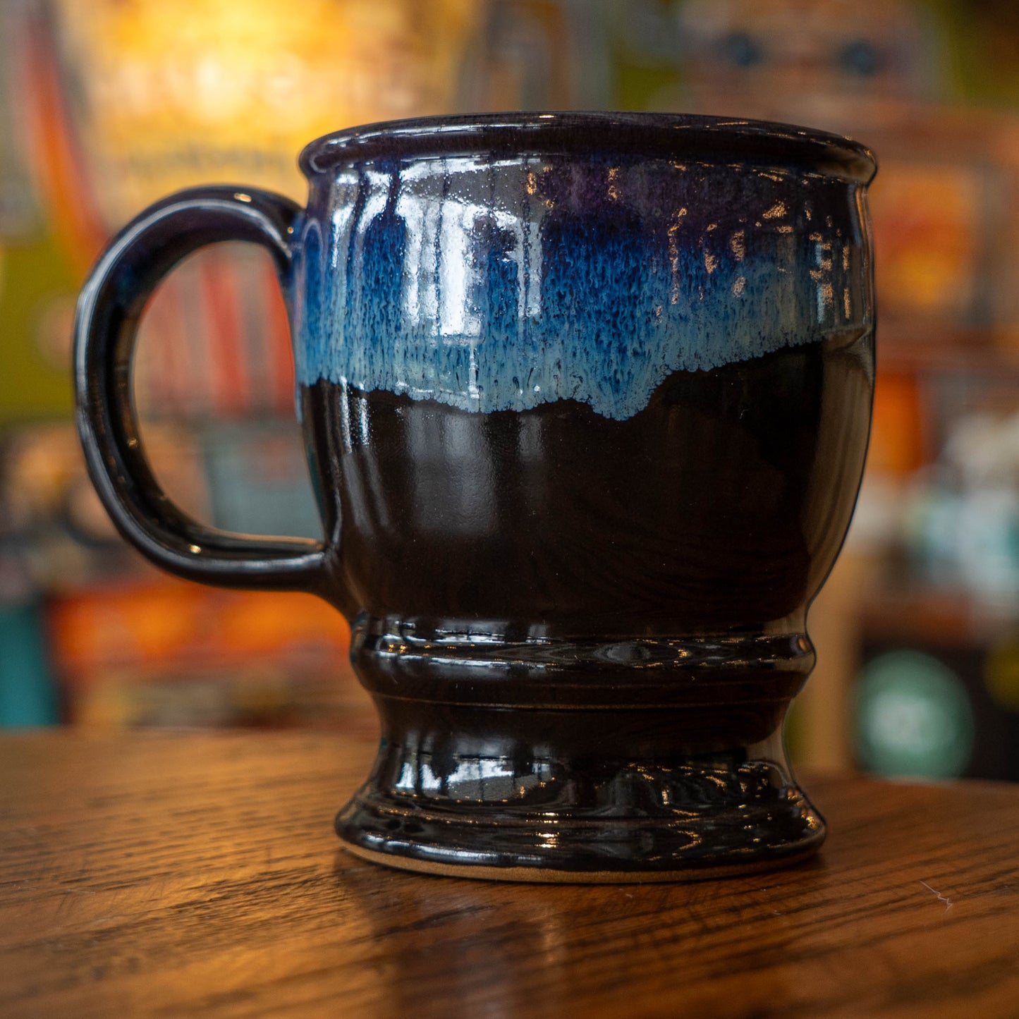 Backside view of Dogfish Head x Grateful Dead Black ceramic mug. The base of the mug is black and halfway turns into a blue gradient oil spill pattern, like a blue sunset. 