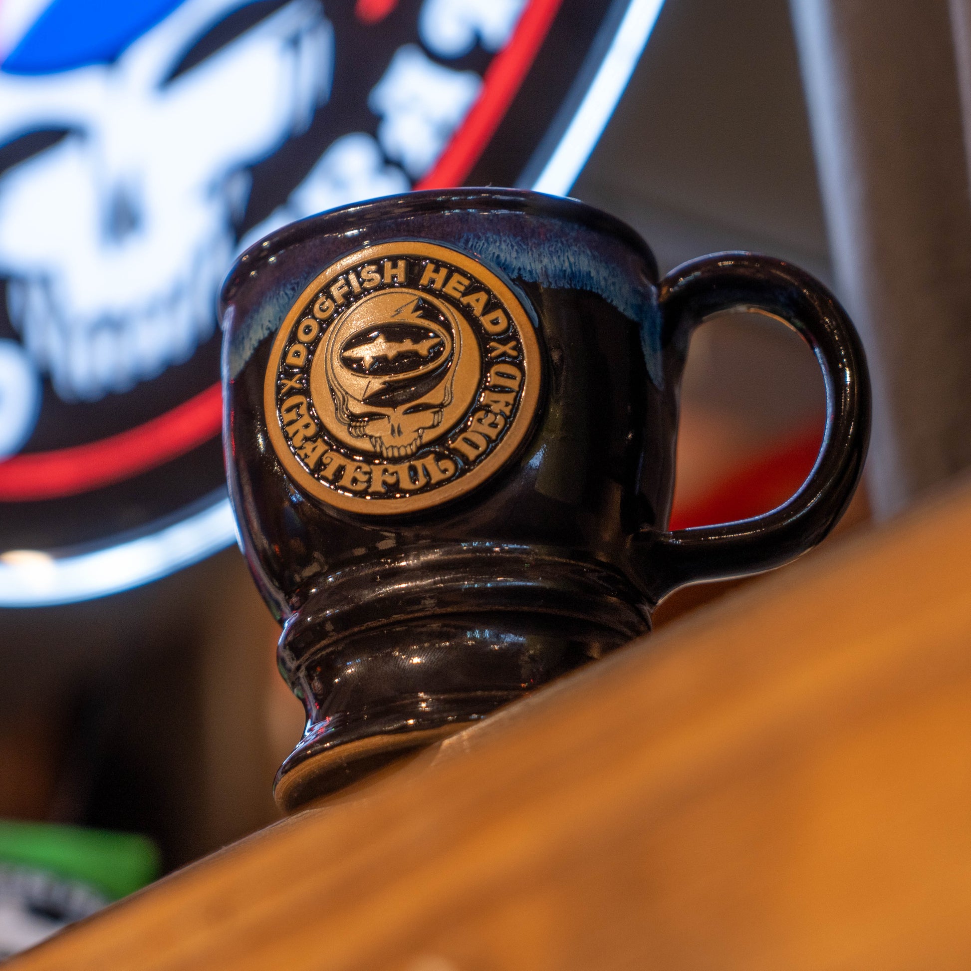 Black and blue ceramic mug with a brown Dogfish Head x Grateful Dead logo sitting on a bar 
