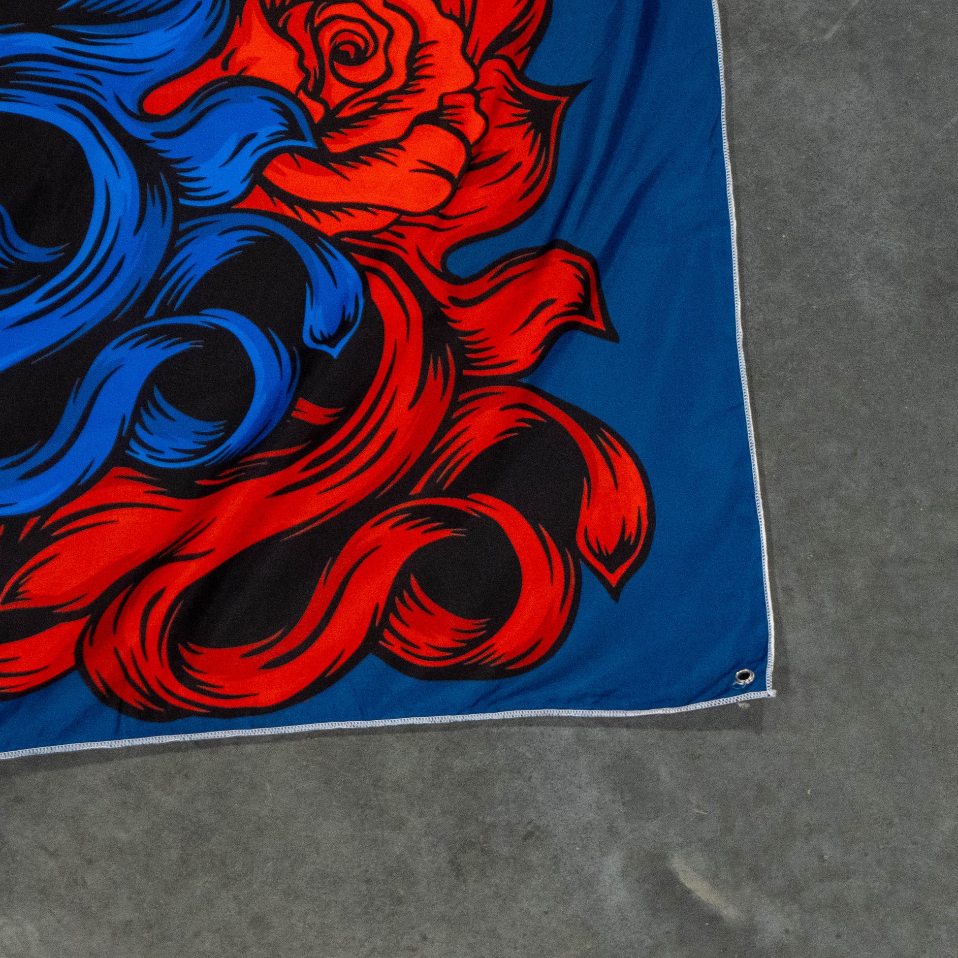 A close-up of the Merchtank Dogfish Head x Grateful Dead Flag Tapestry, featuring bold red and blue abstract roses with swirling designs on a blue background, reminiscent of classic Grateful Dead memorabilia.