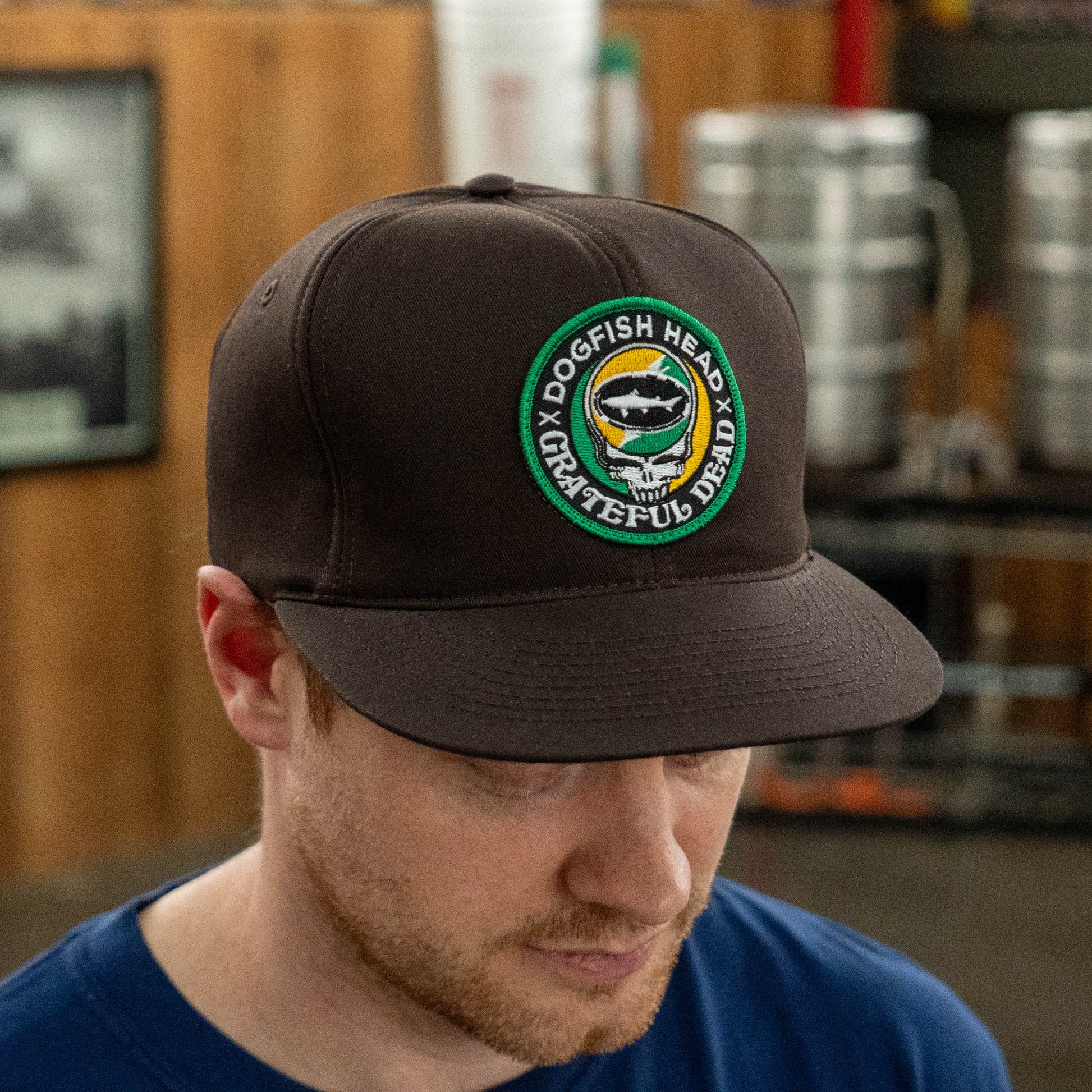 Dogfish Head x Grateful Dead espresso foam baseball hat worn by model, featuring and embroidered green and orange patch and retro flat brim