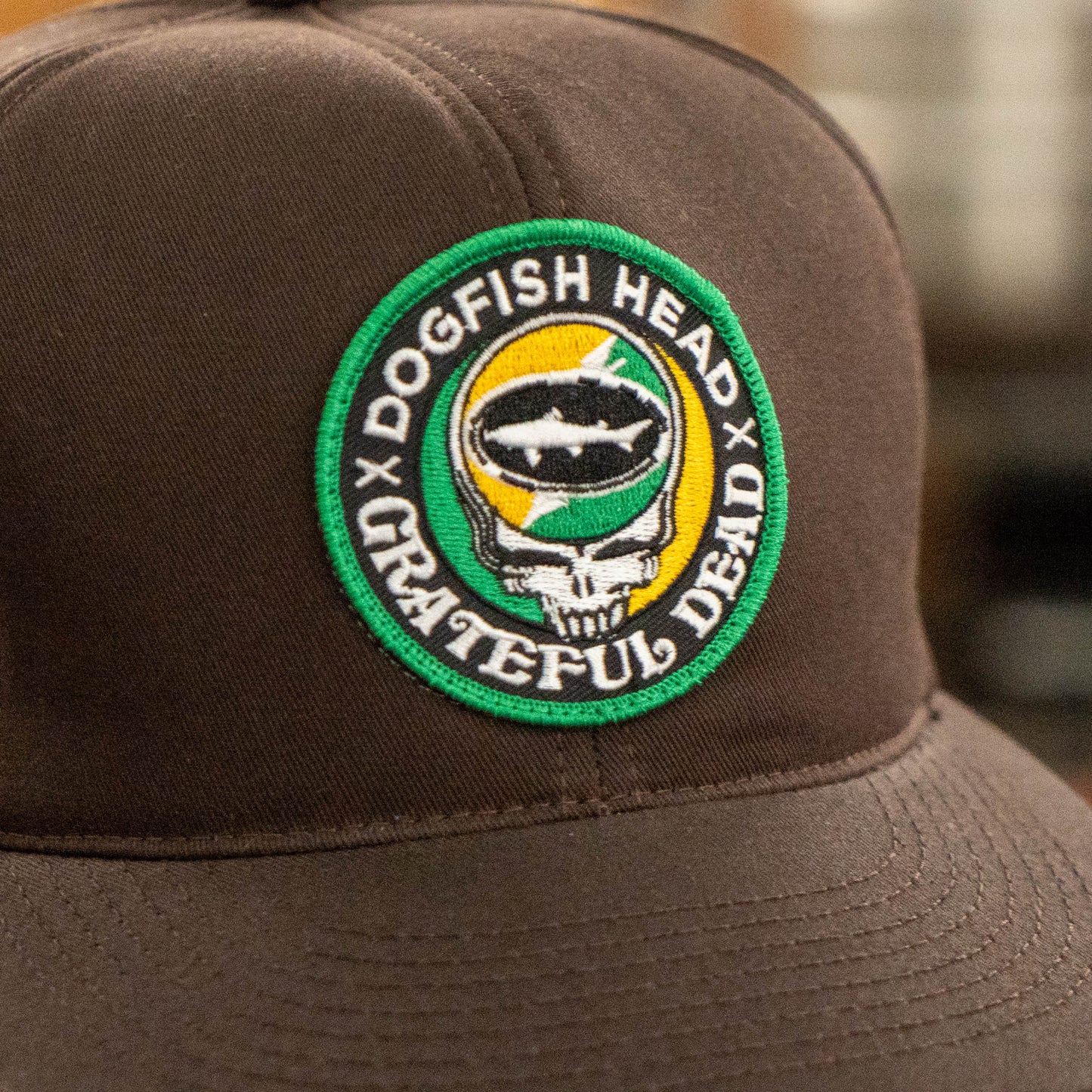Close-up of green and orange embroidered Dogfish Head x Grateful Dead logo patch on espresso brown retro foam baseball hat.