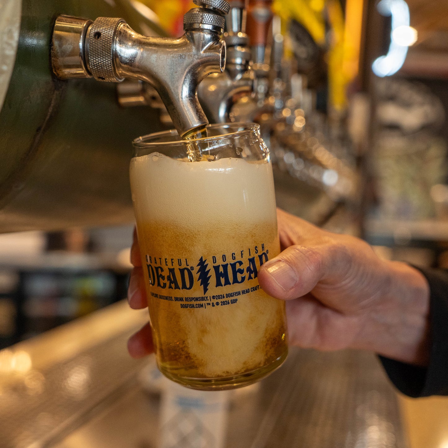 Beer being poured into Dogfish Head x Grateful Dead 2026 RSD can glass at brewery tap, showcasing collaboration logo.