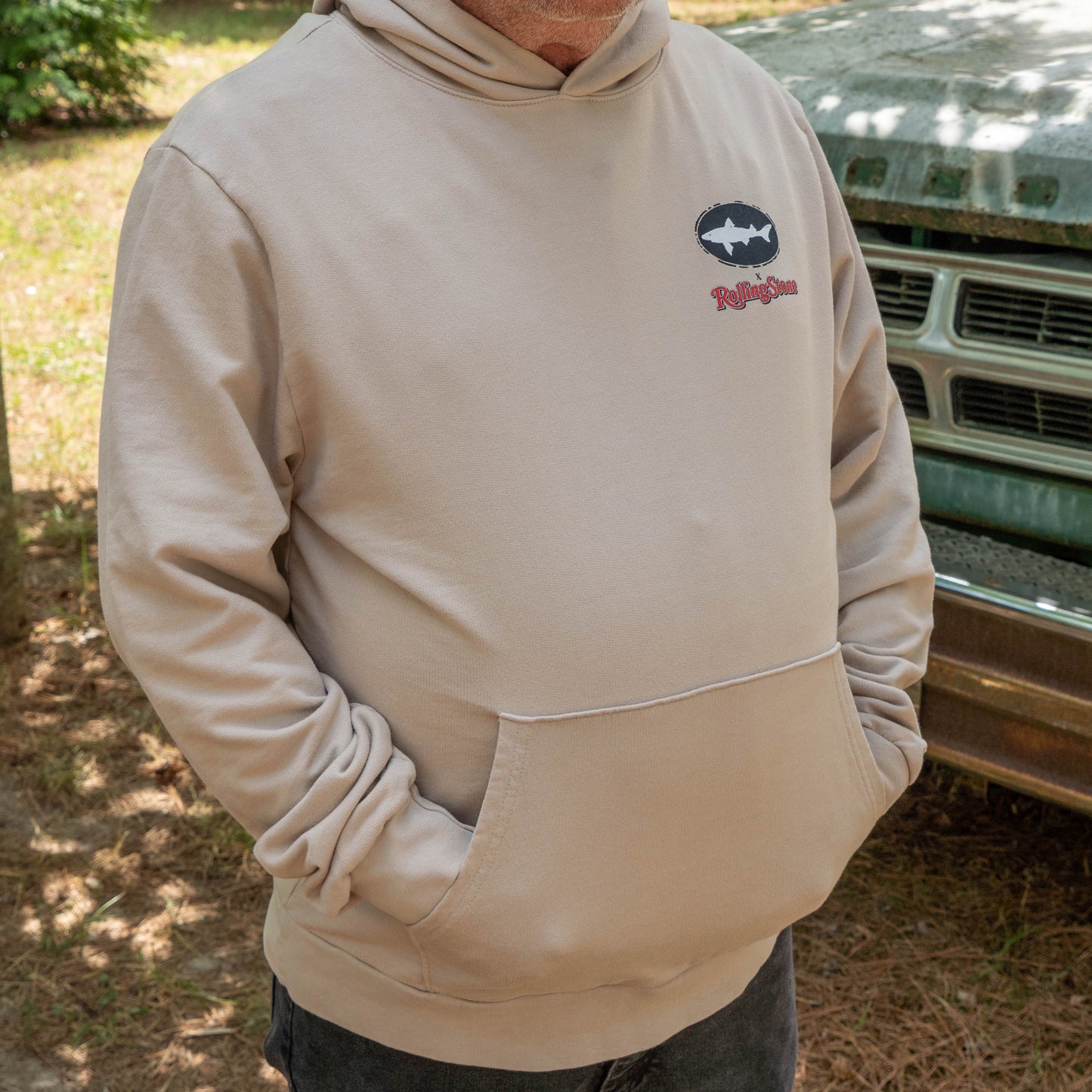 Person wearing Dogfish Head x Rolling Stone Mocha Hoodie  featuring a black oval Dogfish logo logo a white shark and red Rolling Stone logo