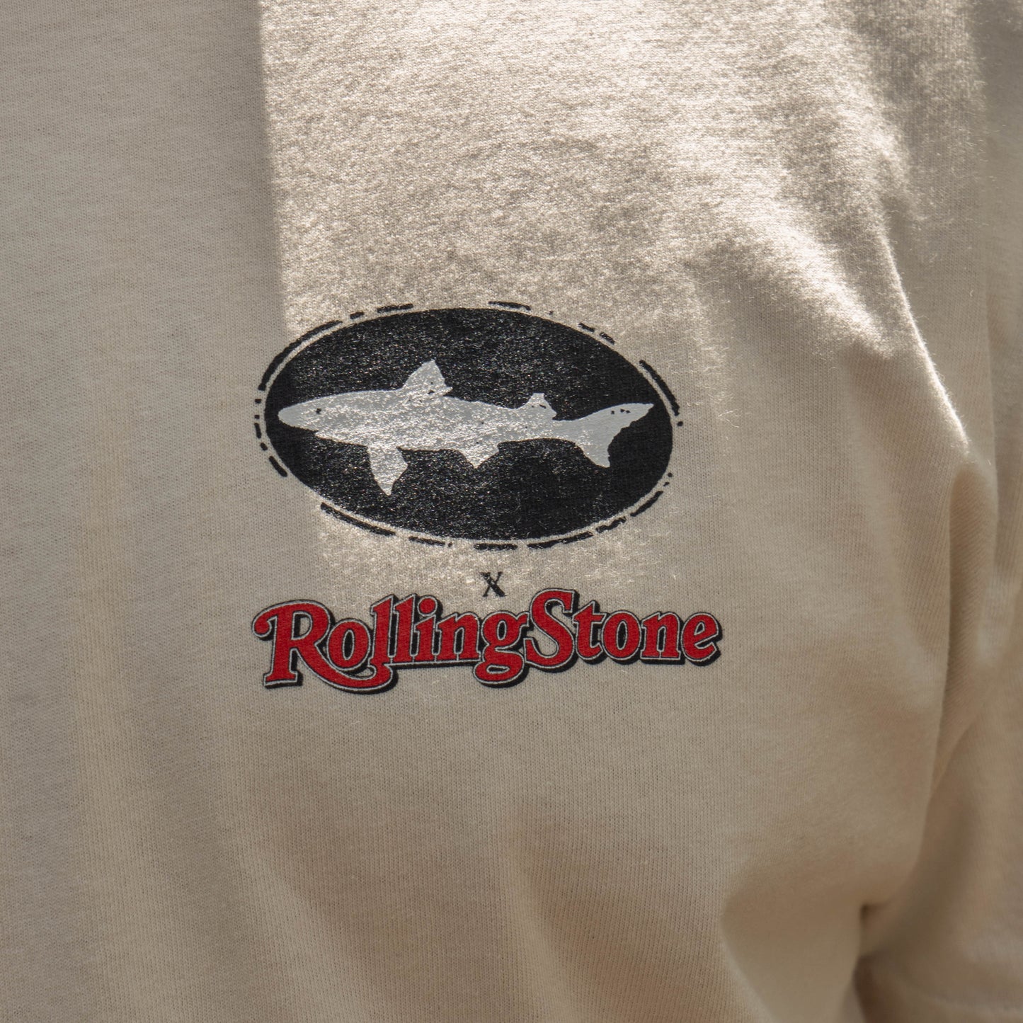 The Dogfish Head x Rolling Stone Oatmeal Tee with a black oval and white shark Dogfish Head logo above the red Rolling Stone logo