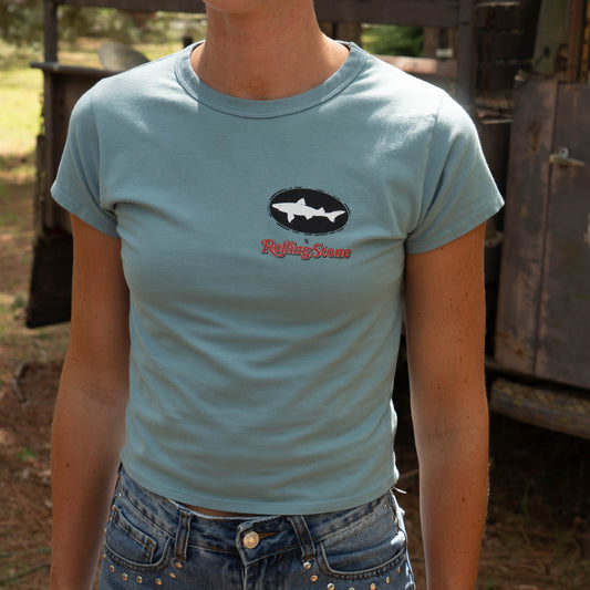Outdoors, someone wears the Dogfish Head x Rolling Stone Women's Slate Blue Baby Tee Shirt with blue jeans 
