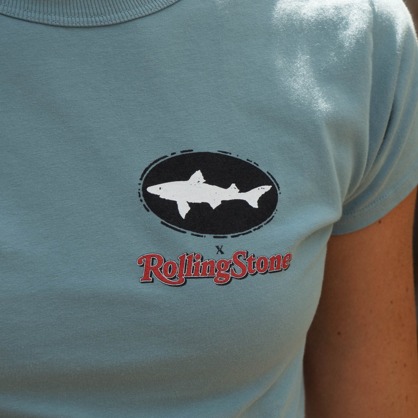 Dogfish Head x Rolling Stone Women's Slate Blue Baby Tee Shirt  with a black Dogfish Head logo and a  red Rolling Stone logo on the left chest