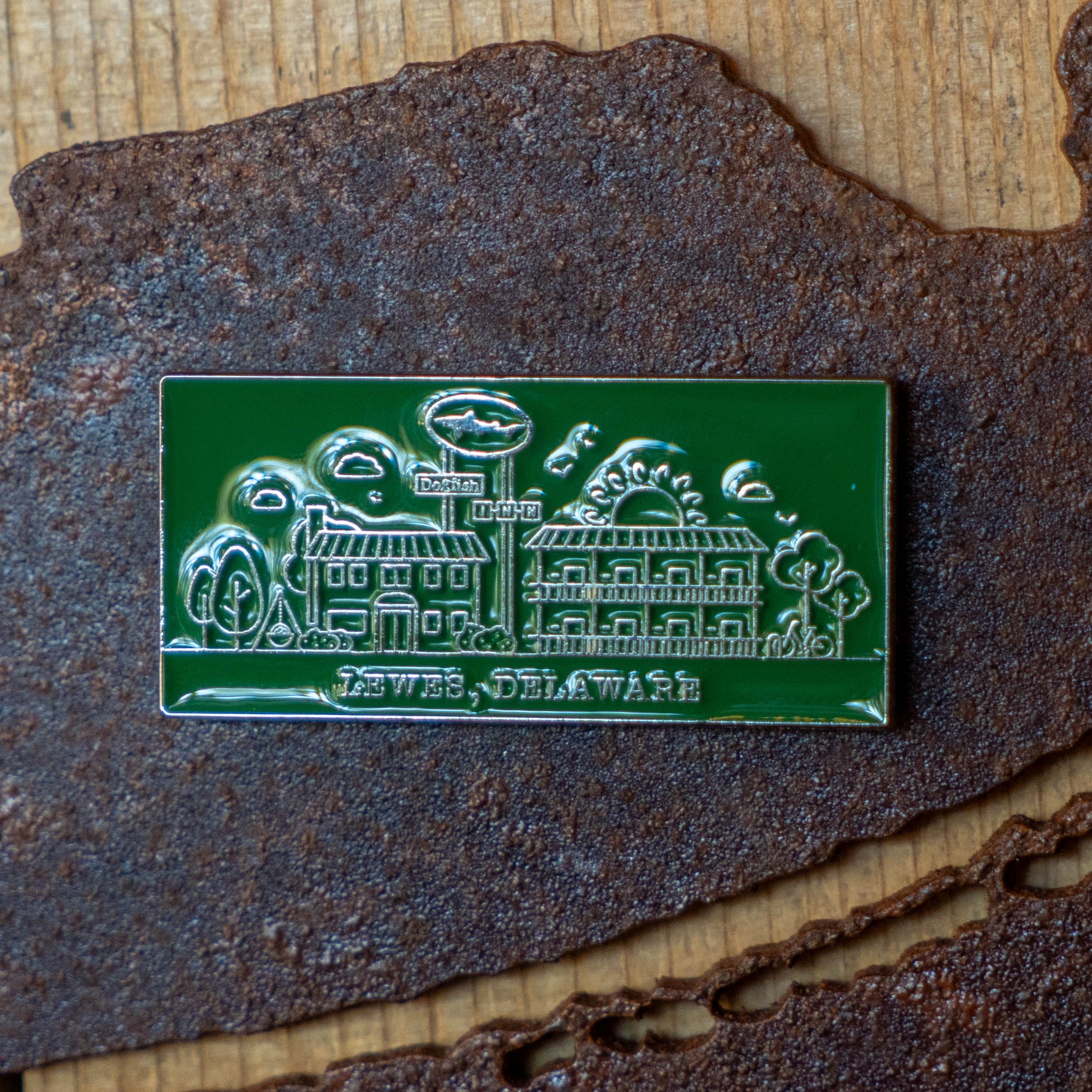 The Enamel Inn Magnet by Arrasmith Promotions LLC showcases Lewes, Delaware with engraved buildings, trees, and clouds on a green background—ideal for Dogfish Head fans or as a standout collectible magnet.