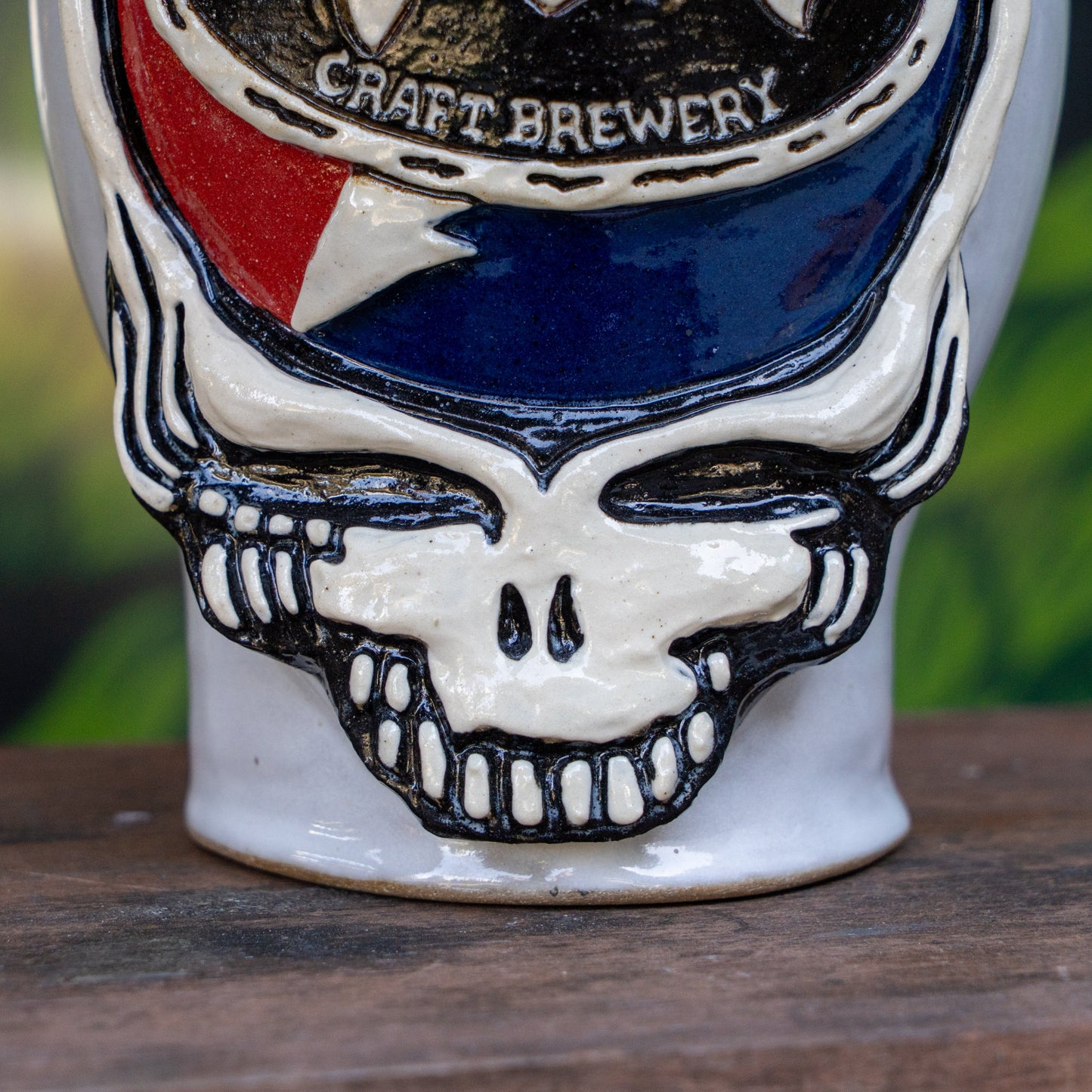 The Uber Growler by Romanick Pottery is a ceramic mug with a raised grinning skull, its top half in red, white, and blue, plus "Craft Brewery" on a banner above—echoing the look of a handmade growler.