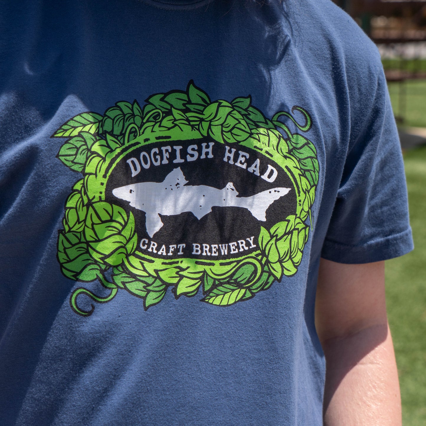 A person wears the GO WEST T-SHIRT COMPANY's “Midnight Got a Minute? Tee Shirt,” showcasing its unique design as they stand outdoors on fresh green grass.