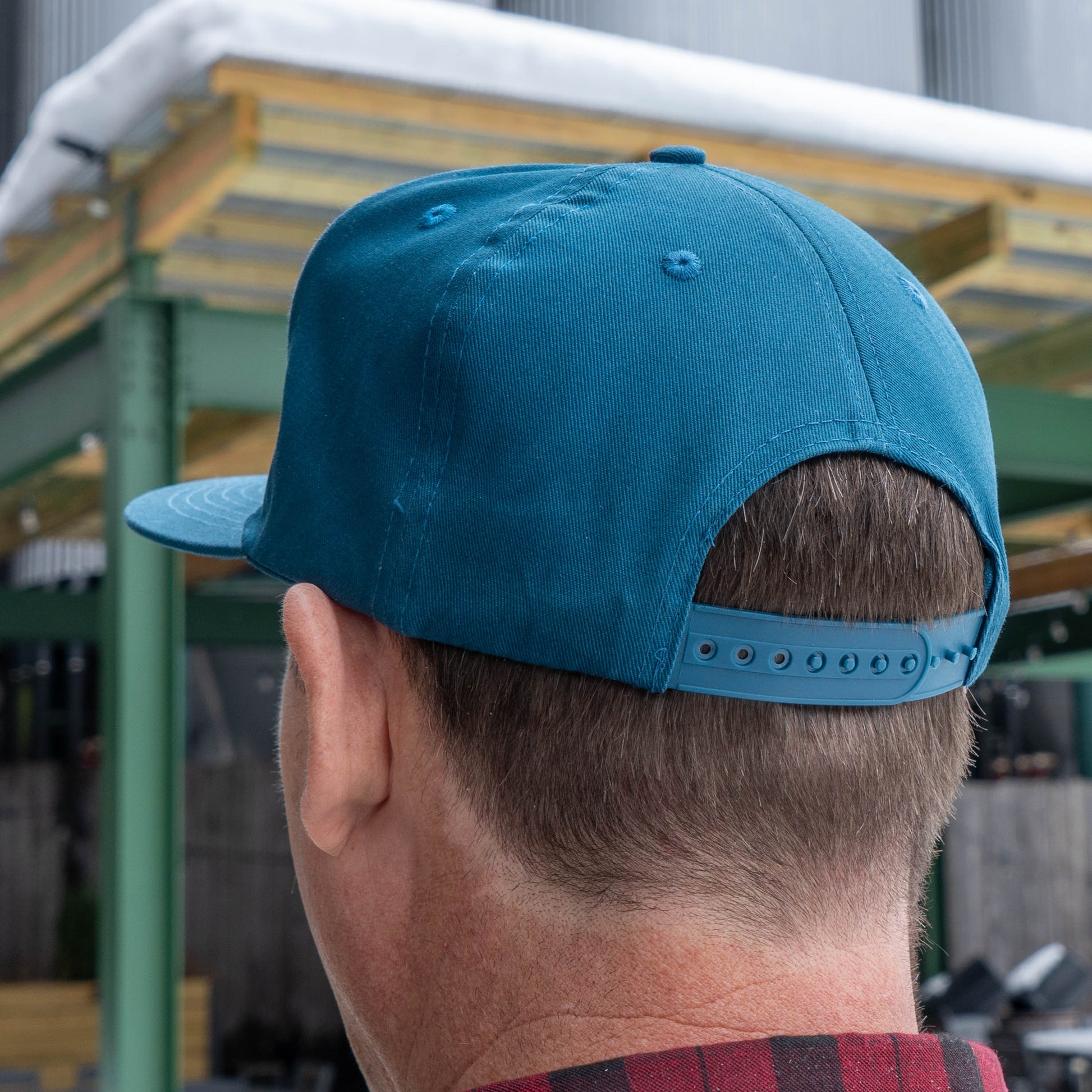 Backside view of a man wearing the Music Month Trucker Hat, shows cerulean blue back panels and adjustable snap back. 