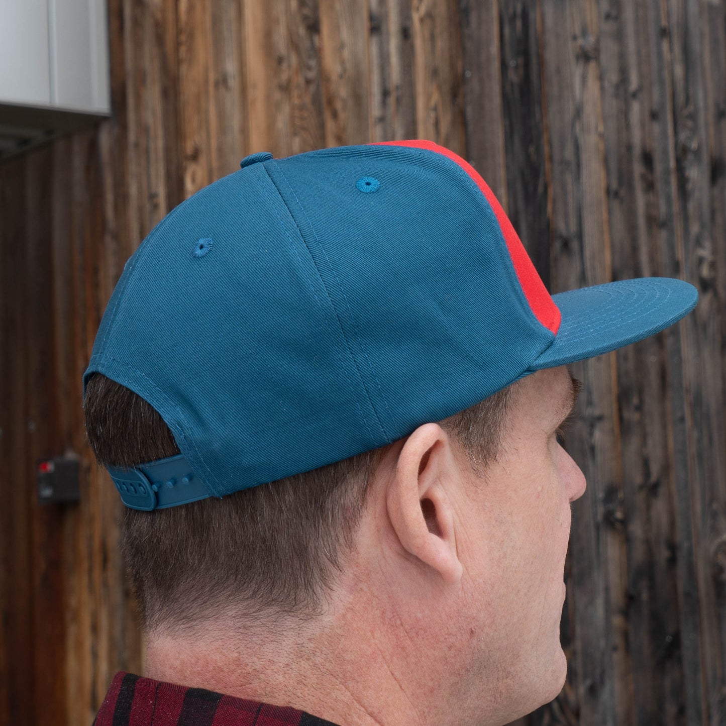 Side view of man wearing Music Month Trucker Hat. Shows cerulean blue back and side panels and red front panels 