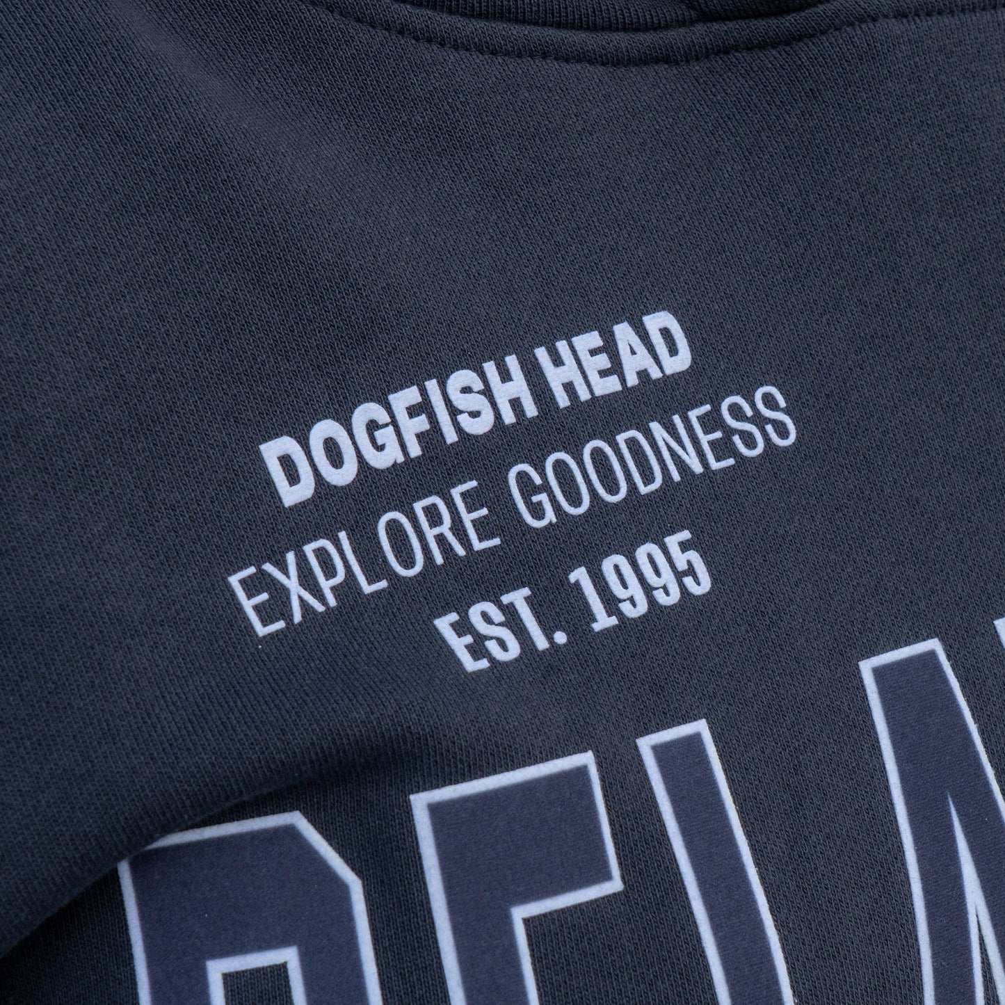 Close up of white text on left chest that reads, "Dogfish Head, Explore Goodness, Est. 1995."
