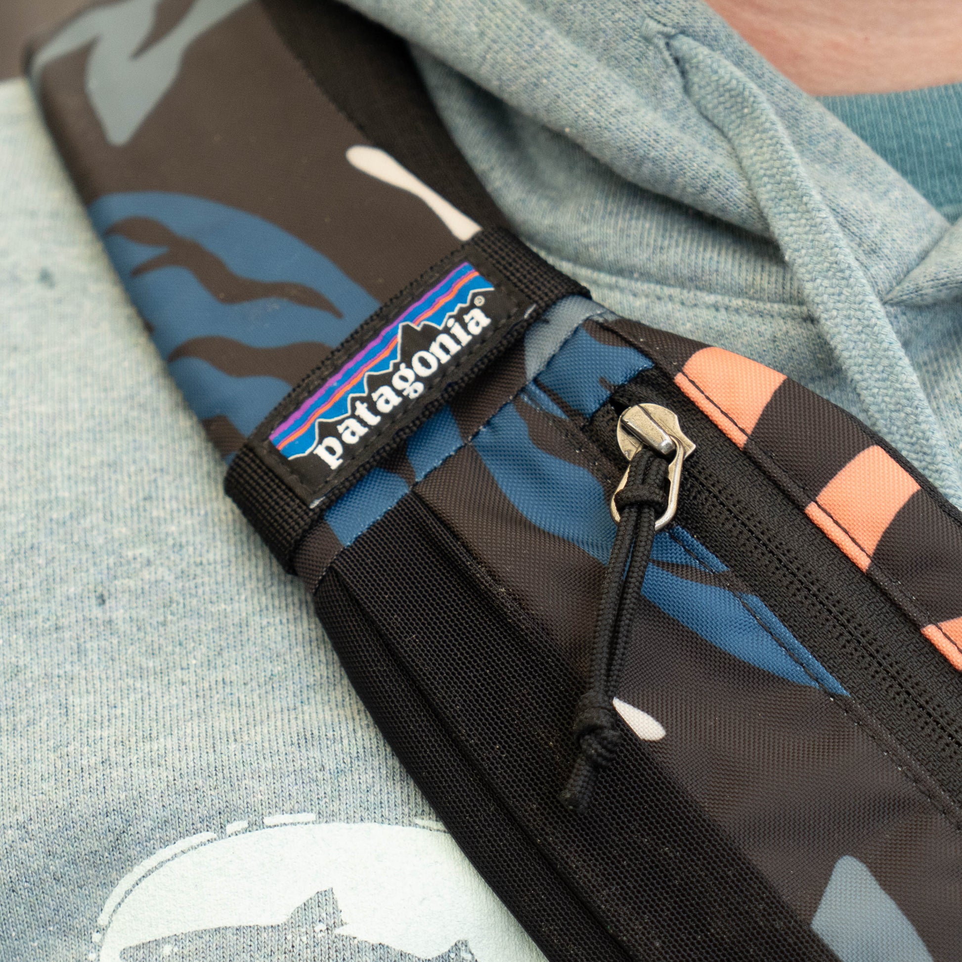 Close-up of Patagonia Atom Sling 8L strap with logo tag and zipper detail, durable camo fabric crossbody daypack design