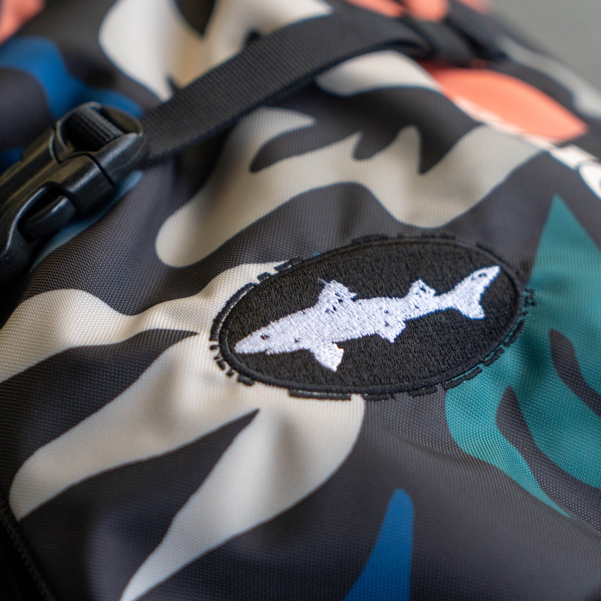 Close-up of Patagonia Atom Sling 8L camo crossbody bag with embroidered dogfish head patch and durable ripstop fabric, outdoor everyday carry detail