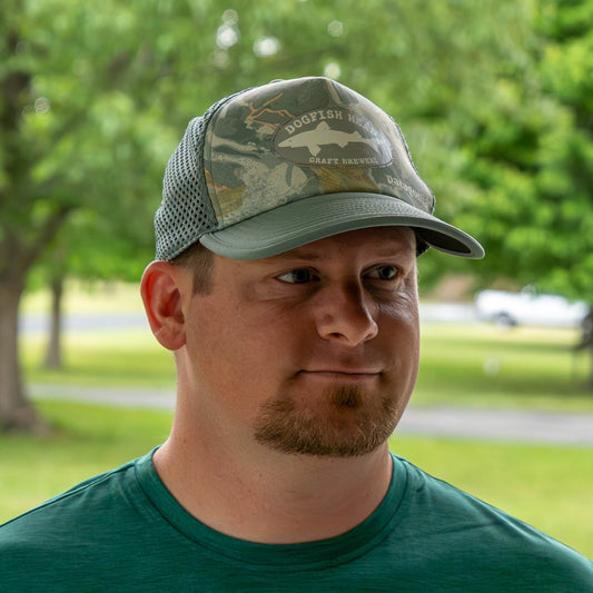 Man wearing a Dogfish Head Patagonia duckbill trucker hat with camouflage pattern and Dogfish Head Craft brewery logo