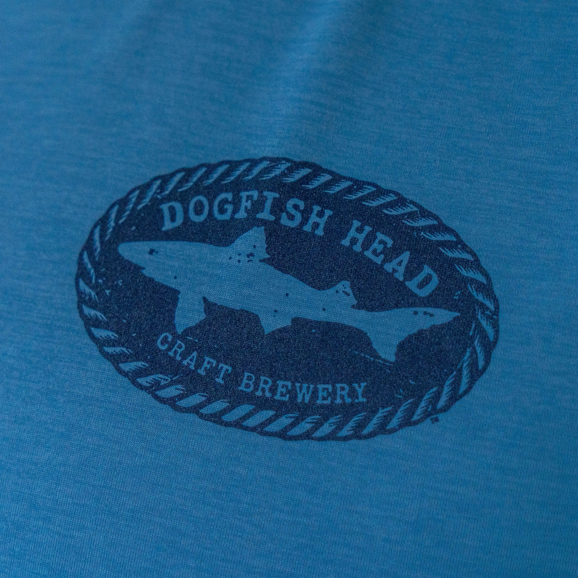 Close-up of Dogfish Head craft brewery shark logo on blue Patagonia sleeveless Cap Cool Daily shirt, soft breathable fabric